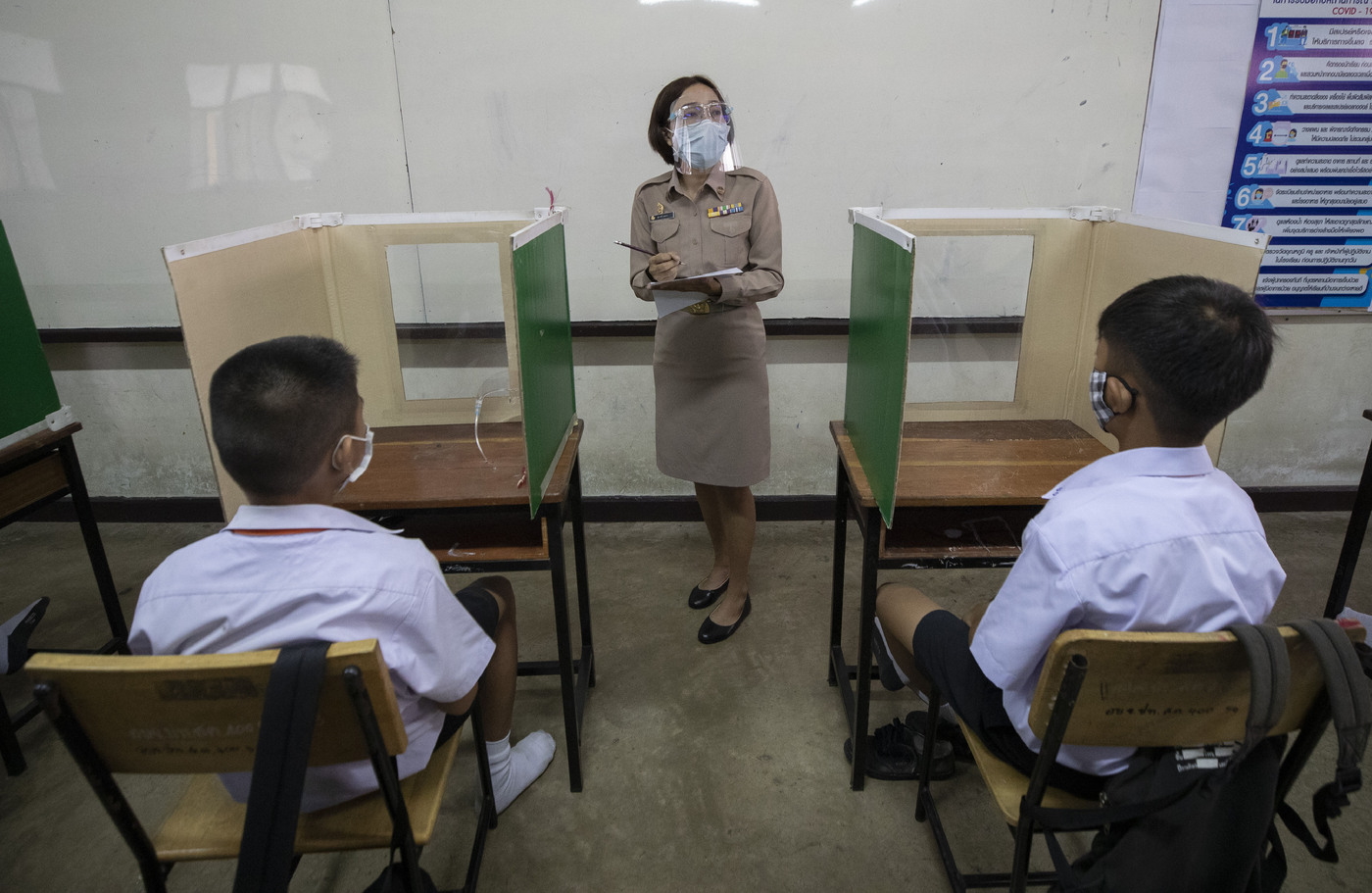 A teacher in protective gear teaches her students, seated at partitioned desks at the Samkhok School in Pathum Thani, outside Bangkok, Wednesday, July 1, 2020. Thailand has begun a fifth phase of relaxations of COVID-19 restrictions, allowing the reopening of schools and high-risk entertainment venues such as pubs and massage parlors that had been shut since mid-March. (AP Photo/Sakchai Lalit)