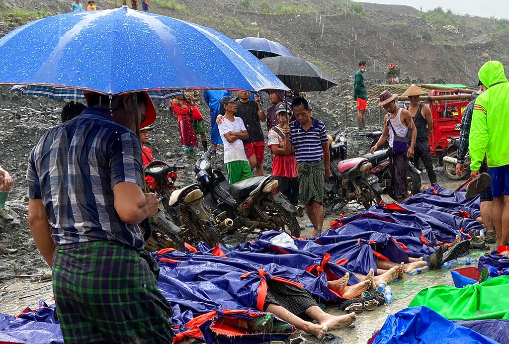 People walk and gather near dead bodies of jade scavengers who were killed in a landslide covered with plastic and lined up near a jade mining area Thursday, July 2, 2020, in Hpakant, Kachine state in northern Myanmar. Myanmar government says a landslide at a jade mine in the country’s north has killed 50 people. The Ministry of Information cited the local fire service at the site of Thursday’s landslide in Hpakant in Kachin state.(AP Photo/Zaw Moe Htet)