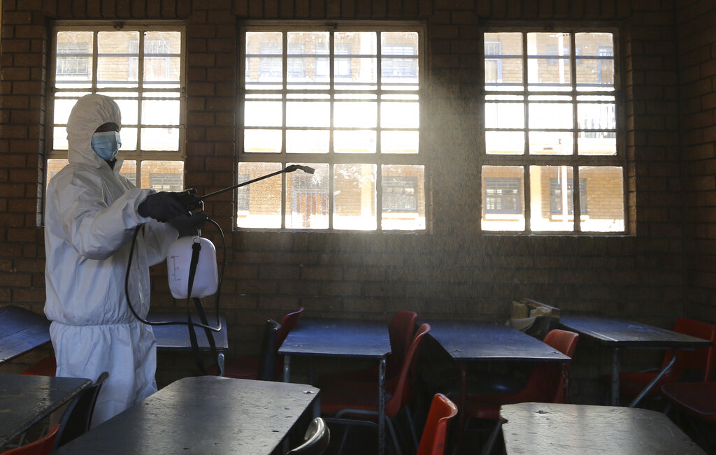 FILE - In this May 26, 2020, file photo, a worker from Bidvest Prestige wearing personal protective equipment, sprays disinfectant in a classroom to help reduce the spread the coronavirus ahead of the reopening of Landulwazi Comprehensive School, east of Johannesburg, South Africa. The options for African students eager to keep studying while schools remain closed because of the coronavirus pandemic seems varied, but the reality for many is that they will fall behind and possibly drop out of school forever, worsening inequality on an already unequal continent. (AP Photo/Themba Hadebe, File)