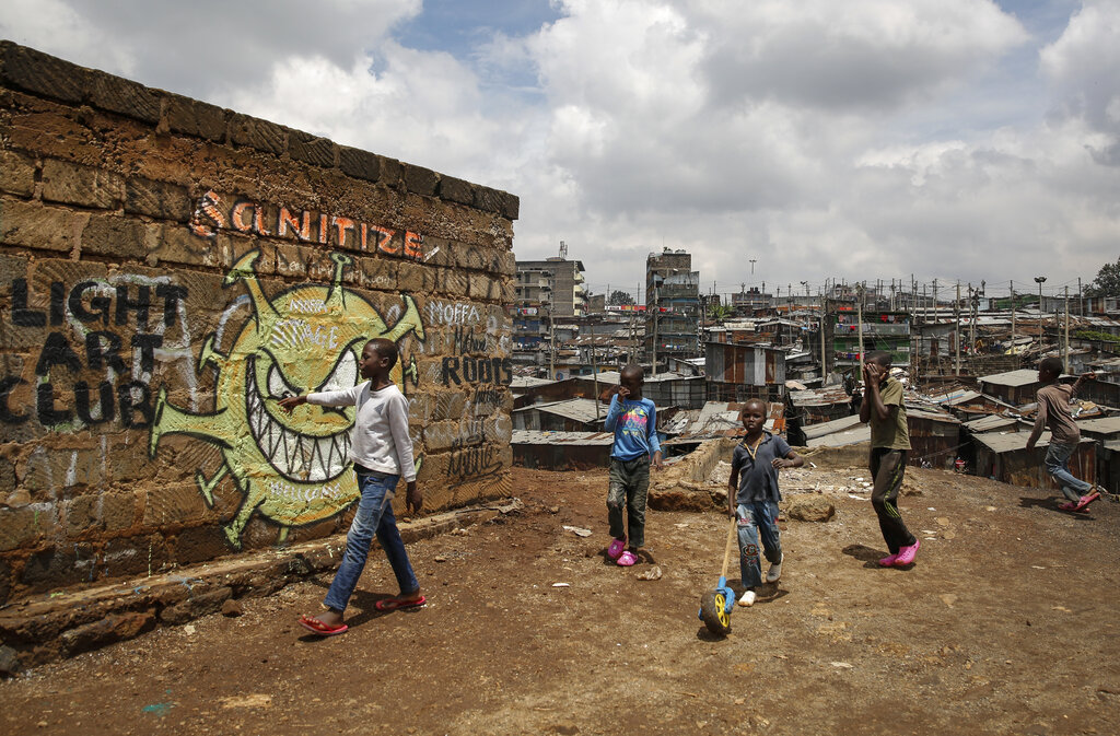 FILE - In this April 22, 2020, file photo, children walk past an informational mural depicting the coronavirus and warning people to sanitize to prevent its spread, painted by graffiti artists from the Mathare Roots youth group, in the Mathare informal settlement, of Nairobi, Kenya. The options for African students eager to keep studying while schools remain closed because of the coronavirus pandemic seems varied, but the reality for many is that they will fall behind and possibly drop out of school forever, worsening inequality on an already unequal continent. (AP Photo/Brian Inganga, File)