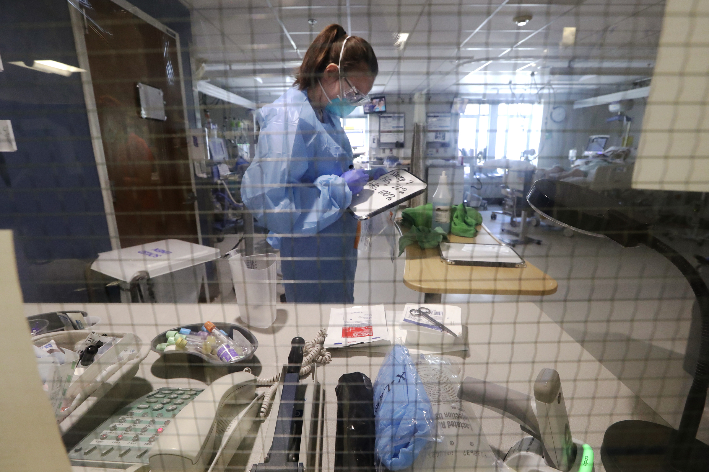 A nurse writes information on a small white board from inside a patient's room before holding it up to a window for another staff member in the COVID-19 Intensive Care Unit at Harborview Medical Center Friday, May 8, 2020, in Seattle. (AP Photo/Elaine Thompson)