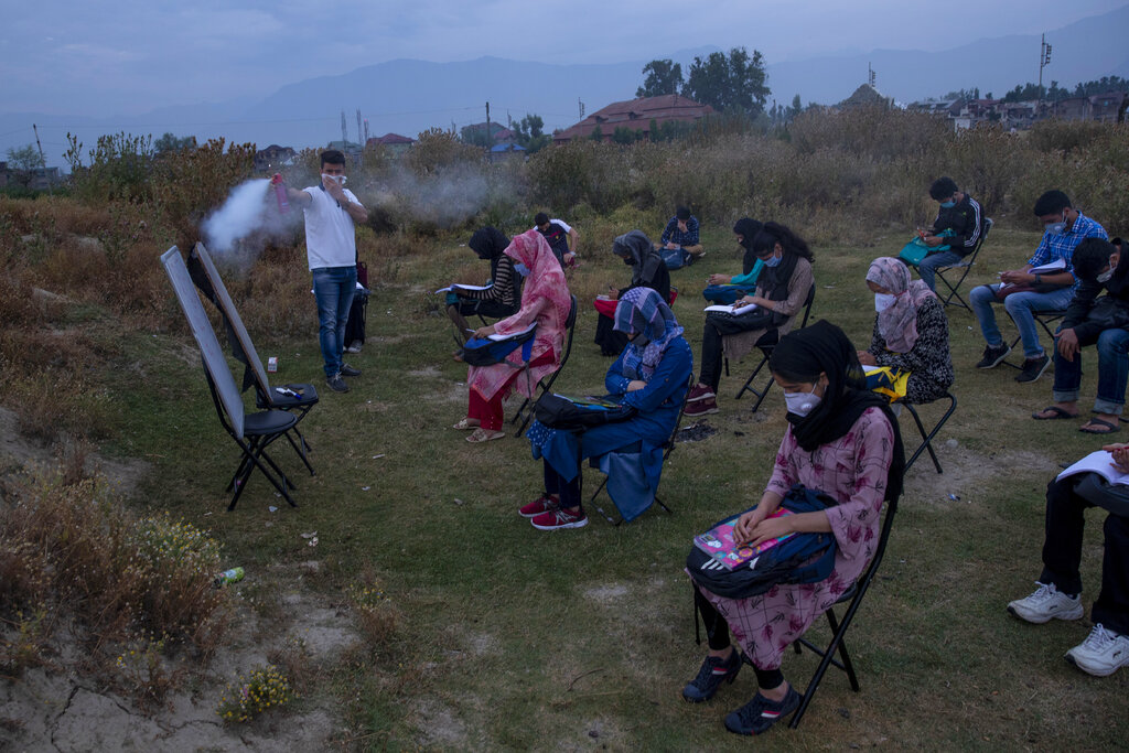 Muneer Alam, an engineer-turned-math teacher, sprays disinfectant before the start of an early morning outdoor class at Eidgah, a ground reserved for Eid prayers, in Srinagar, Indian controlled Kashmir, Friday, July 18, 2020. Alam said the driving force to start the open-air classes was seeing children all around him depressed and anxious. The open-air classroom buzzes with students. Some sit on chairs. Others place themselves on rugged mats or on the ground. Social distancing is maintained. (AP Photo/Dar Yasin)