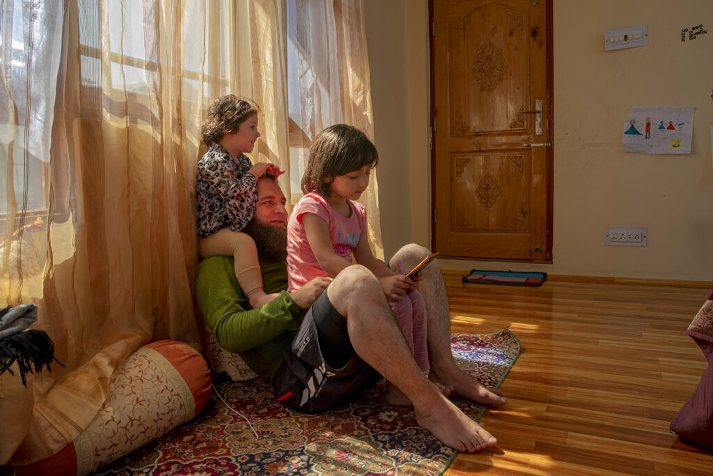 Khalid Bazaz plays with his niece Sundas Irfan, as his daughter Maria Khalid sits on his lap and watches online classes, at their home in Srinagar, Indian controlled Kashmir, Thursday, July 23, 2020. Confined to their homes, students have found it challenging to study online with the painstakingly slow internet connections, which also faces outages following the frequent gunbattles between rebels and Indian soldiers. With no high-speed internet, many educators are unable to upload video lectures and conduct online classes. But some are making the best of limited resources. 