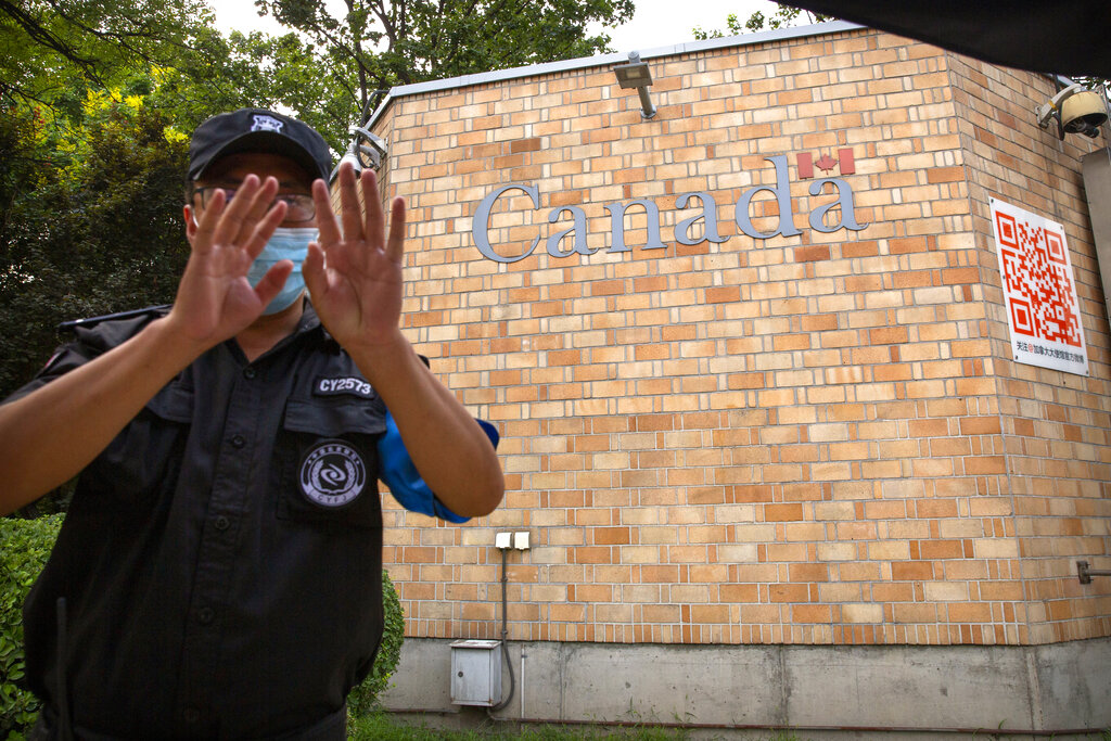 A security officer wearing a face mask to help protect against the coronavirus gestures outside the Canadian Embassy in Beijing, Thursday, Aug. 6, 2020. China has sentenced a Canadian citizen to death on charges of manufacturing the drug ketamine amid heightened tension between the two countries. (AP Photo/Mark Schiefelbein)