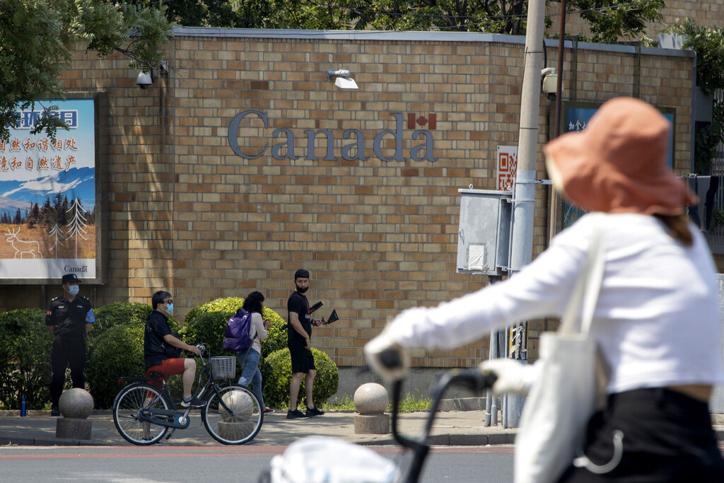 A security guard stands on duty as residents pass by the Canadian Embassy in Beijing on Friday, June 19, 2020. Chinese prosecutors charged two detained Canadians with spying Friday in an apparent bid to step up pressure on Canada to drop a U.S. extradition request for a Huawei executive under house arrest in Vancouver. (AP Photo/Ng Han Guan)