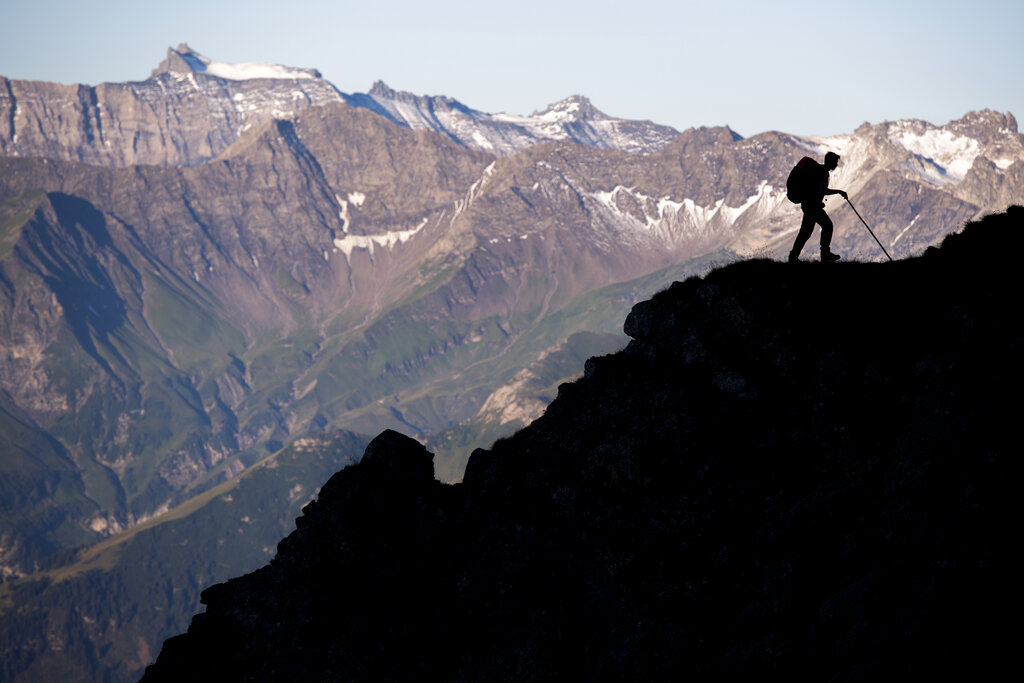 A sheperd is on his way as a flock of sheep is crossing alpine terrain on Friday, August 7, 2020, under the 