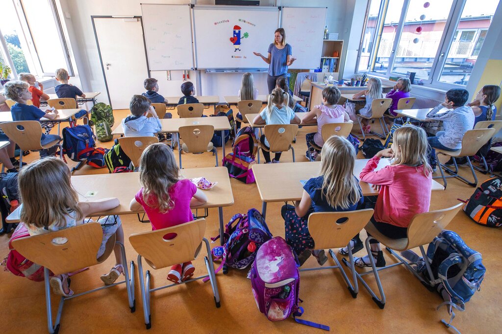 File---File picture taken Aug.3, 2020 shows teacher Francie Keller welcoming the pupils of class 3c in her classroom in the Lankow primary school to the first school day after the summer holidays in Schwerin, Germany. 2020. As Germany’s 16 states start sending millions of children back to school in the middle of the global coronavirus pandemic, those used to the country’s famous “Ordnung” are instead looking at uncertainty, with a hodgepodge of regional regulations that officials acknowledge may or may not work. (Jens Buettner/dpa via AP, File)