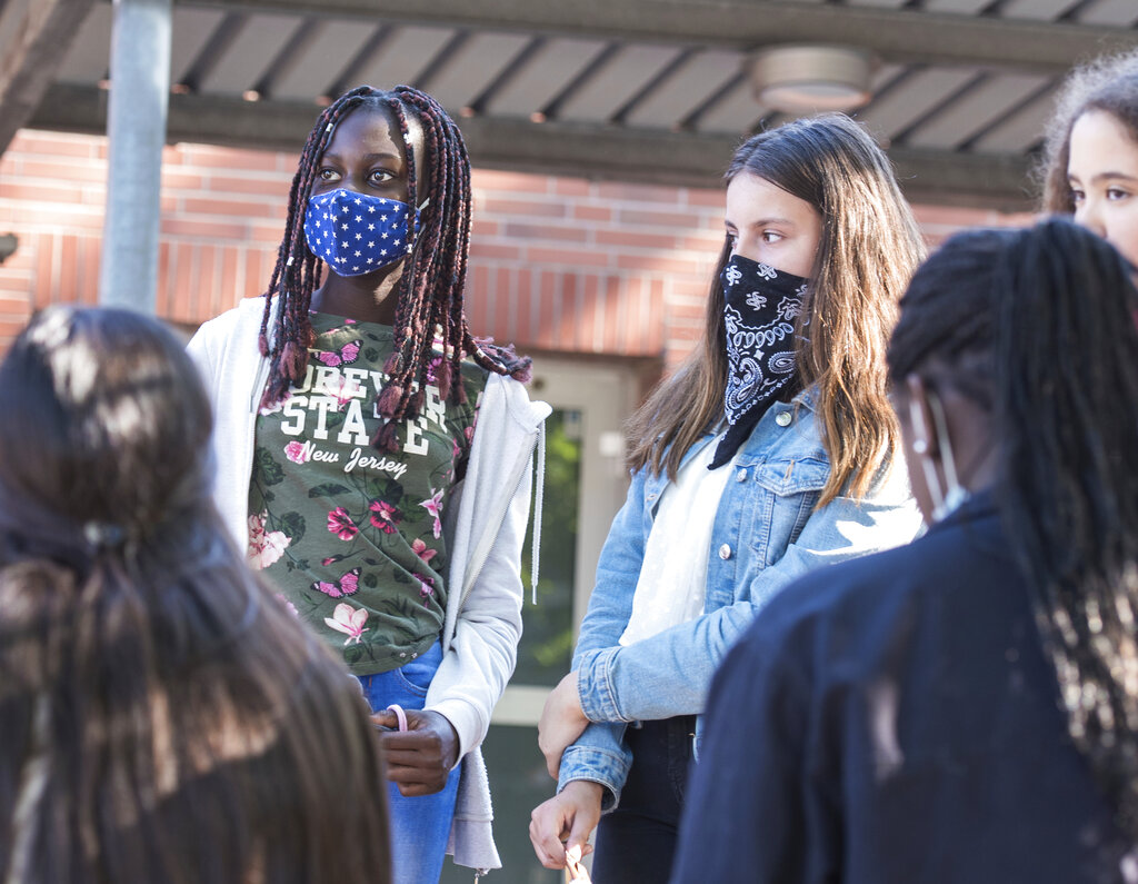 Pupils of a 7th grade of the Max-Schmeling-Stadtteilschule talk to each other with mouth and nose covers in the schoolyard in Hamburg, Germany, Thursday, Aug.6, 2020. As Germany’s 16 states start sending millions of children back to school in the middle of the global coronavirus pandemic, those used to the country’s famous “Ordnung” are instead looking at uncertainty, with a hodgepodge of regional regulations that officials acknowledge may or may not work.(Daniel Bockwoldt/dpa via AP)