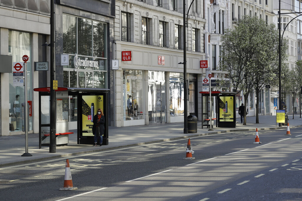 FILE  - In this Tuesday, March 24, 2020 file photo, a woman wearing a face mask to protect against coronavirus, waits at a bus stop on a deserted Oxford Street in London. Unemployment across the U.K. has held steady during the coronavirus lockdown as a result of a government salary support scheme, but there are clear signals emerging that job losses will skyrocket over coming months. The Office for National Statistics said Thursday, July 16, 2020 there were 649,000 fewer people, or 2.2%, on payroll in June when compared with March when the lockdown restrictions were imposed.  (AP Photo/Matt Dunham, File)