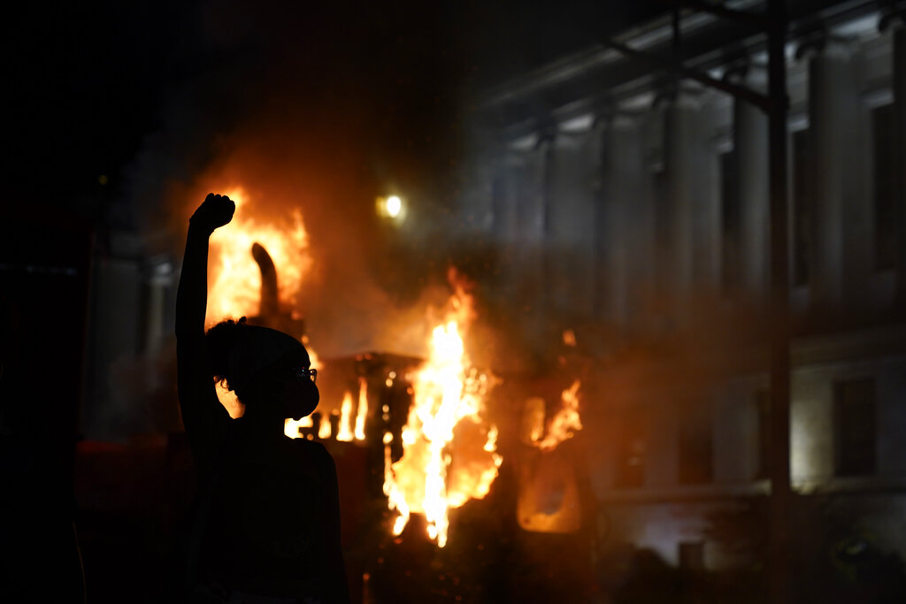 FILE - In this Aug. 24, 2020, file photo, a protester stands in a cloud of tear gas near a burning garbage truck outside the Kenosha County Courthouse, in Kenosha, Wis. Until the police shooting of Jacob Blake, the bedroom community of Kenosha has been largely untouched by the level of demonstrations that had been seen in nearby Milwaukee and Chicago since the death of George Floyd. (AP Photo/David Goldman, File)