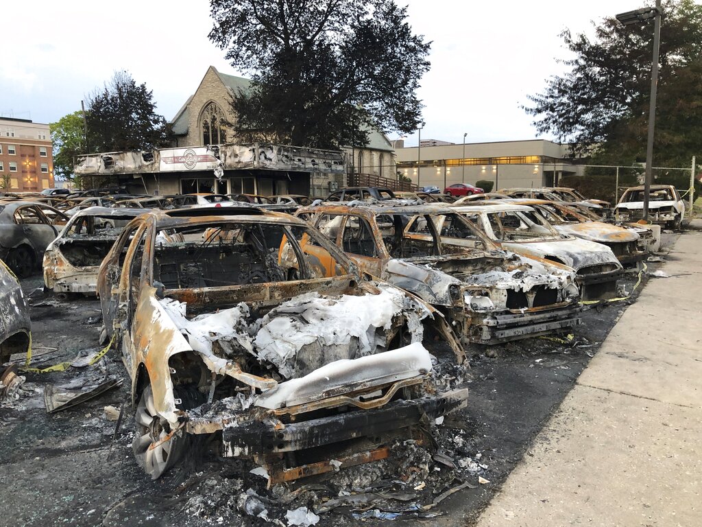 Cars torched during violent protests this week in Kenosha, Wis., sit Thursday, Aug. 27, 2020, as demonstrators gather across the street to speak out against the Sunday police shooting of Jacob Blake. (AP Photo/Russell Contreras)