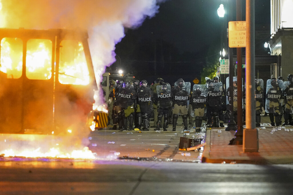 FILE - In this Aug. 24, 2020 file photo, police stand near a garbage truck ablaze during protests over the shooting of Jacob Blake in Kenosha, Wis. In the span of 48 hours, two Black men in U.S. cities hundreds of miles apart were shot by police in episodes that set off a national conversation about the need for officers to open fire on people walking away from them.  (AP Photo/Morry Gash, File)