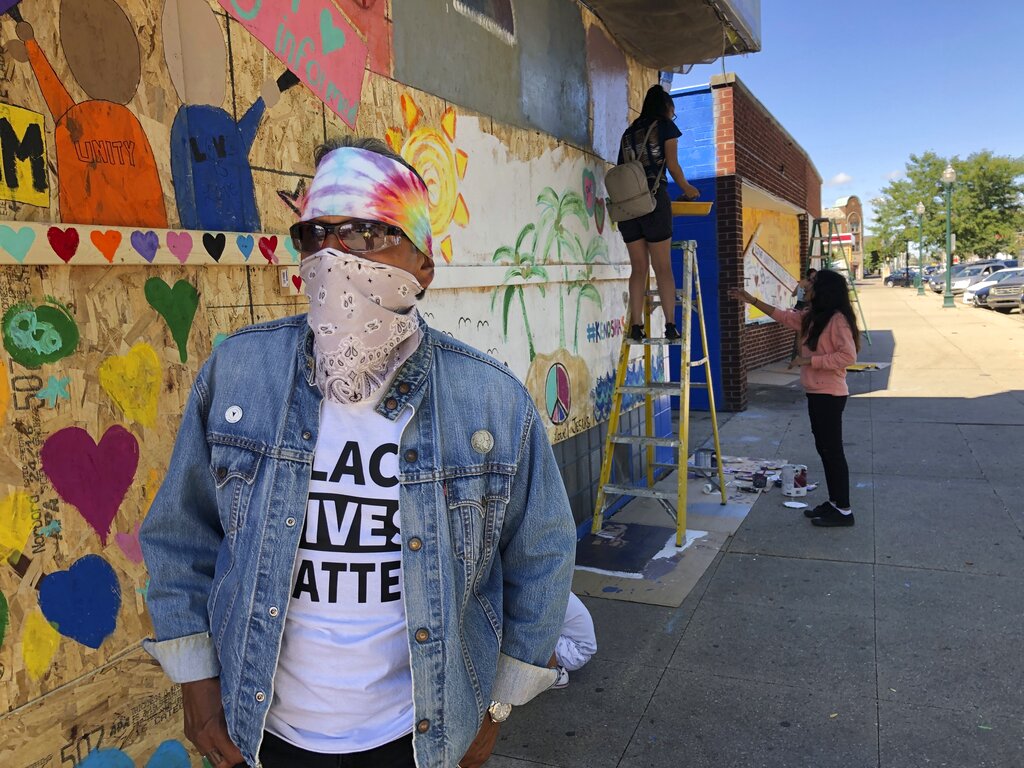 David Sanchez, 66, a long-time Kenosha, Wis., resident, watches volunteers paint murals on boarded-up businesses on Sunday, Aug. 30, 2020. The businesses were affected by recent violent protests following the police shooting of Jacob Blake. (AP Photo/ Russell Contreras)