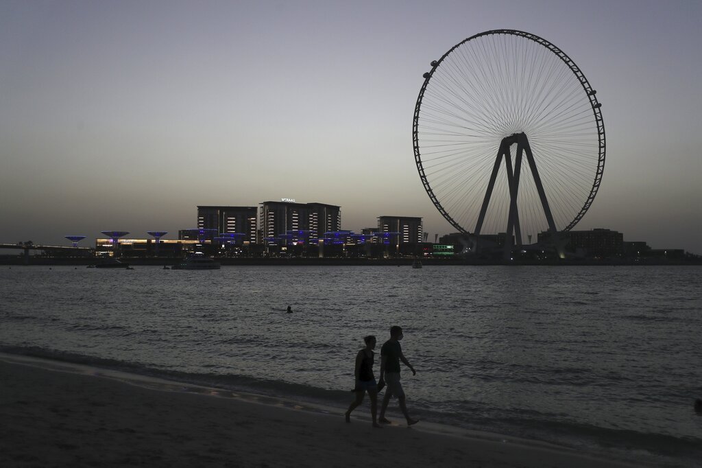 A couple walk on the beachfront of the Persian Gulf with a backdrop of the 