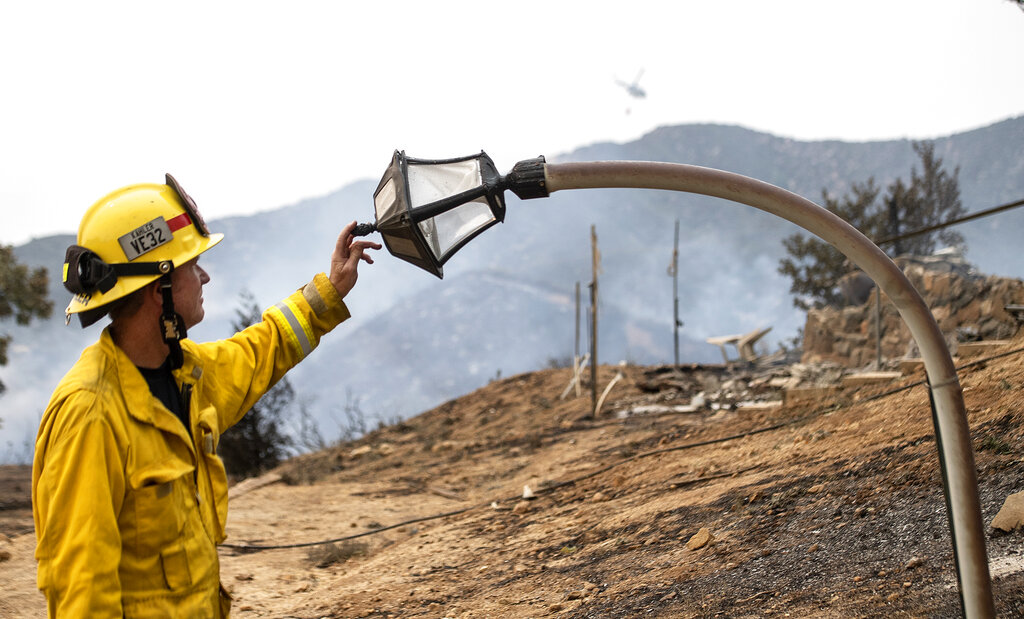 Fire engineer, Paul Kahler, of Fountain Valley, Cailf., examines a melted light post where a structure was destroyed by the El Dorado wildfire near Yucaipa, Cailf., on Monday, Sept. 7, 2020, A couple's plan to reveal their baby's gender went up not in blue or pink smoke but in flames when the device they used sparked a wildfire east of Los Angeles. The fire started Saturday morning in dry grasses at El Dorado Ranch Park, a rugged natural area in the city of Yucaipa. (Cindy Yamanaka/The Orange County Register/SCNG via AP)