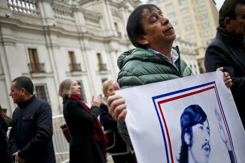 Segundo Almonacid holds a banner with portrait of his brother Luis Almonacid, who was detained and continues missing after Chile's military coup, outside La Moneda presidential palace on the anniversary of the 1973 military coup in Santiago, Chile, Monday, Sept. 11, 2017. The 1973 military coup ousted democratically elected President Salvador Allende and began the 17-year dictatorship of Gen. Augusto Pinochet. (AP Photo/Esteban Felix)