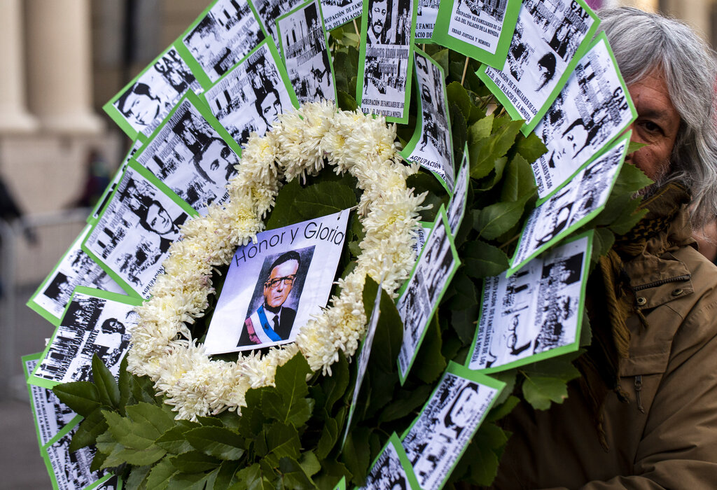 A supporter of the Chile's late President Salvador Allende holds a flower arrangement that will be placed outside the eastern entrance of La Moneda presidential palace on the anniversary of the 1973 military coup and subsequent death of Allende, in Santiago, Chile, Wednesday, Sept. 11, 2019. It was through the eastern entrance that Allende's body was carried by soldiers and firefighters from the destroyed presidential palace 46 year ago during the coup that ousted the democratically elected leader and began the 17-year dictatorship of Gen. Augusto Pinochet. The arrangement is adorned with photos of the victims of the dictatorship as well as a sign on the center with a photo of Allende and text that reads in Spanish 