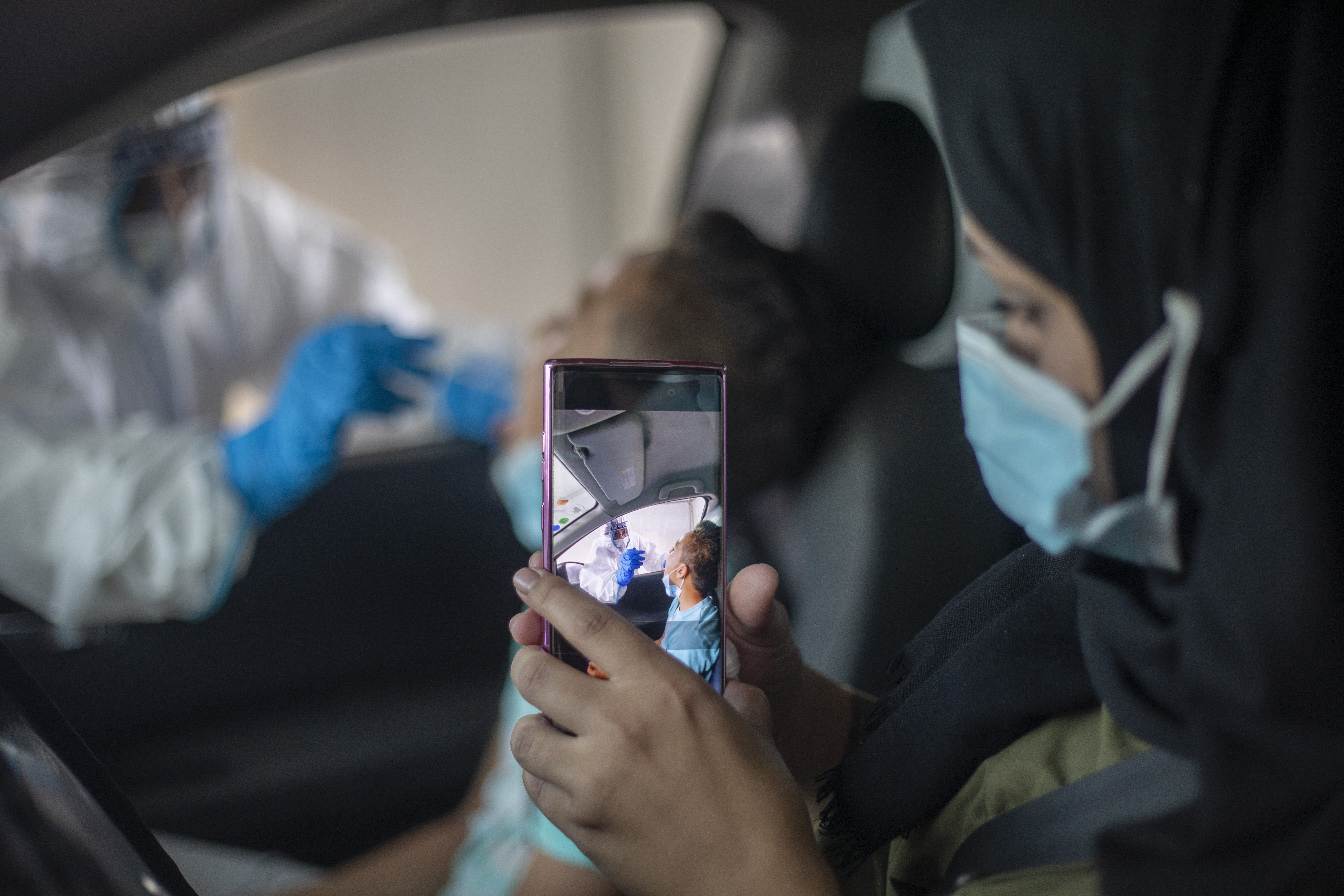 A mother uses a smart phone to capture how her son is tested for Covid-19 by a healthcare worker at a drive-thru COVID-19 testing centre set up at a parking area in east Jerusalem neighborhood of Sheikh Jarrah, Thursday, Sept. 10, 2020. Israel this week imposed new restrictions on some 40 cities and towns with worrying outbreaks, which include nighttime curfews, strict limits on public gatherings and the shuttering of schools. (AP Photo/Ariel Schalit)