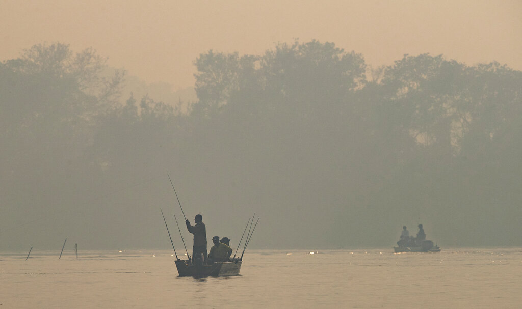 Men fish in the Cuiaba river amid smoke from fires at the Encontro das Aguas park at the Pantanal wetlands near Pocone, Mato Grosso state, Brazil, Sunday, Sept. 13, 2020. A vast swath of the world's largest tropical wetlands is burning in Brazil, sweeping across several national parks and obscuring the sun behind dense smoke. (AP Photo/Andre Penner)