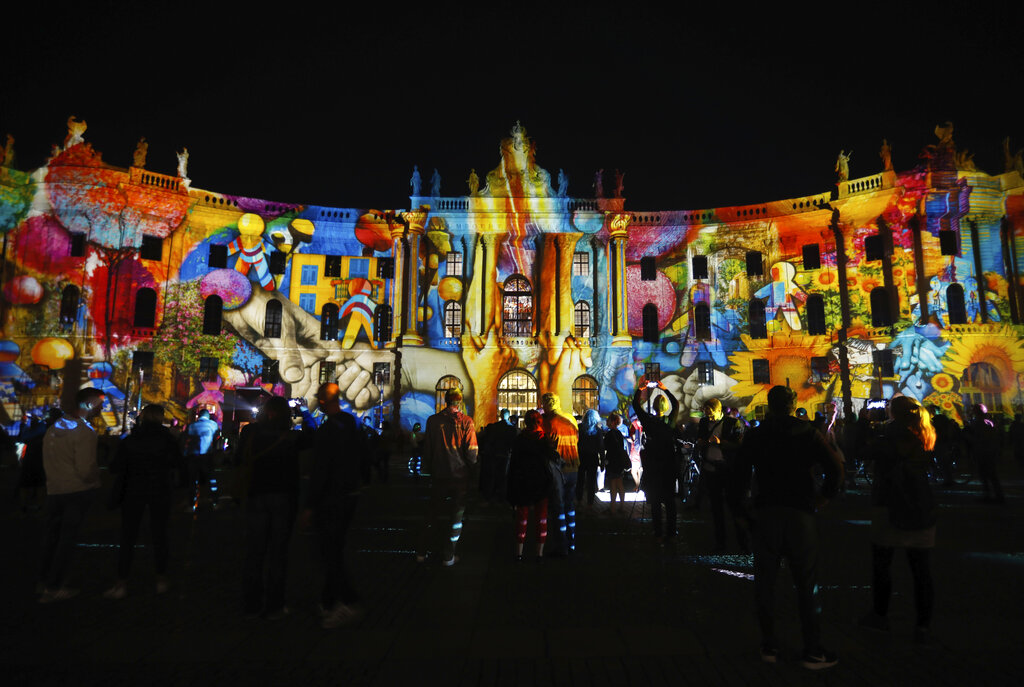 Spectators gather in front of an illuminated building of the Humboldt University during the 'Festival of Lights' event in Berlin, Germany, Friday, Sept. 11, 2020. Berlin's most famous landmarks and buildings will be glowing and sparkling with various colours and types of light and projections during the festival, which runs from Friday Sept. 11 until Sunday, Sept. 20, 2020, at the German capital. (AP Photo/Markus Schreiber)