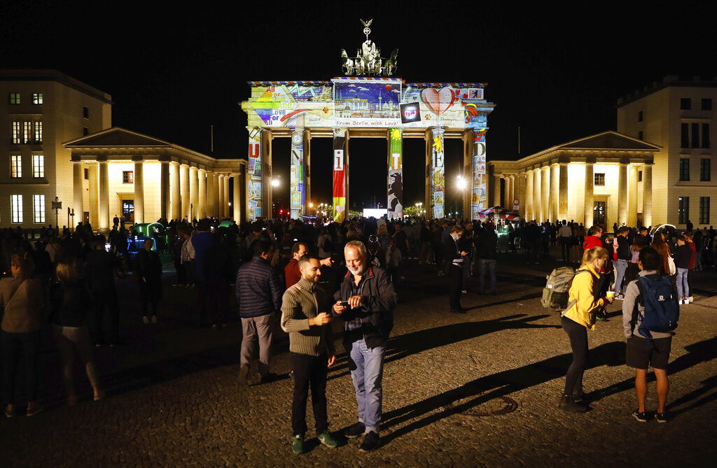 Spectators gather in front of the illuminated Brandenburg Gate during the 'Festival of Lights' event in Berlin, Germany, Friday, Sept. 11, 2020. Berlin's most famous landmarks and buildings will be glowing and sparkling with various colours and types of light and projections during the festival, which runs from Friday Sept. 11 until Sunday, Sept. 20, 2020, at the German capital. (AP Photo/Markus Schreiber)