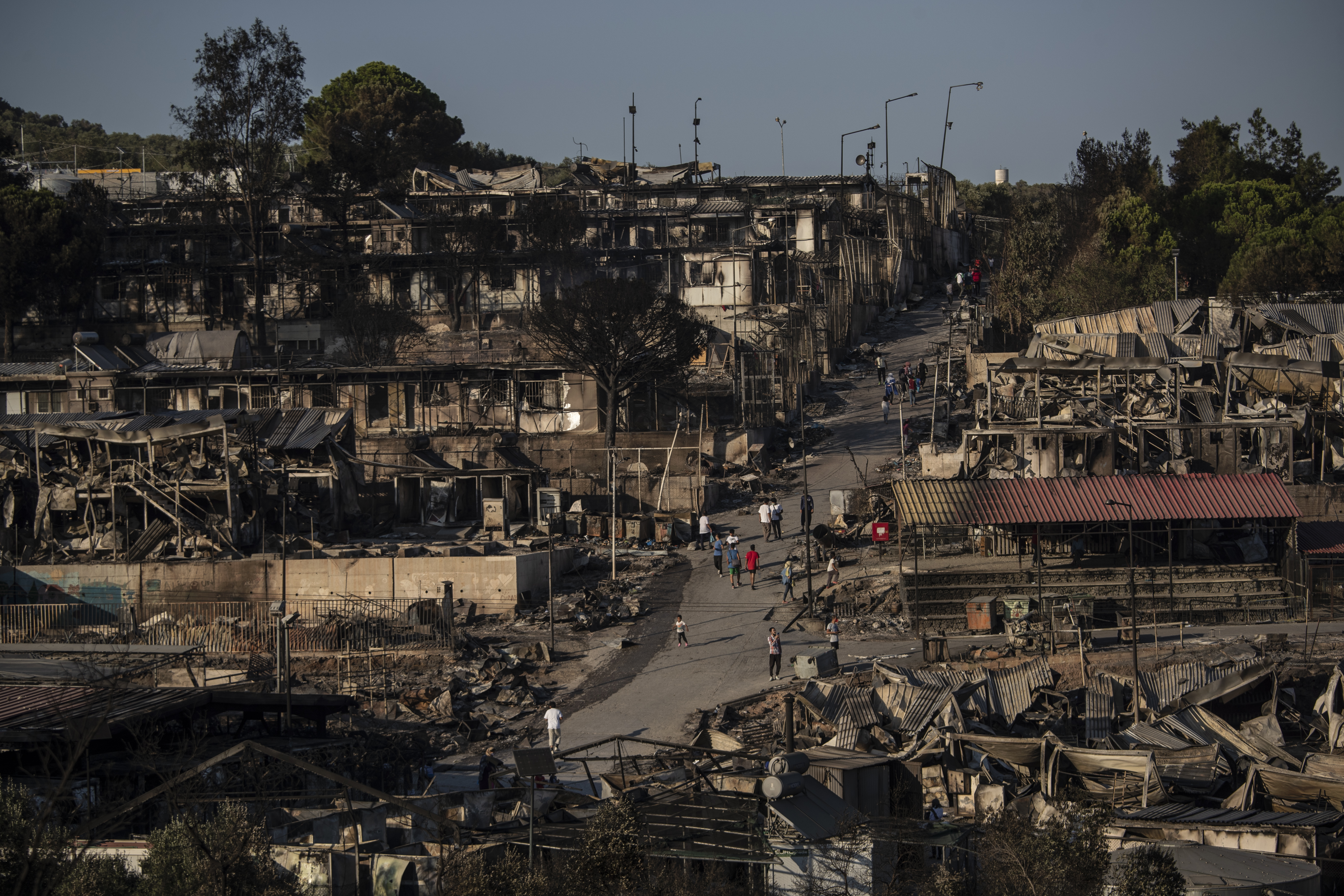 Refugees and migrants walk inside the destroyed Moria camp on Lesbos island, Greece, Wednesday, Sept. 9, 2020. More than 12,000 people were left homeless after fires gutted the sprawling Moria refugee camp. The camp's life ended as it began, in drama: Successive fires that started before dawn on Sept. 9 devastating the site and making 12,000 inhabitants homeless during a COVD-19 lockdown. (AP Photo/Petros Giannakouris)