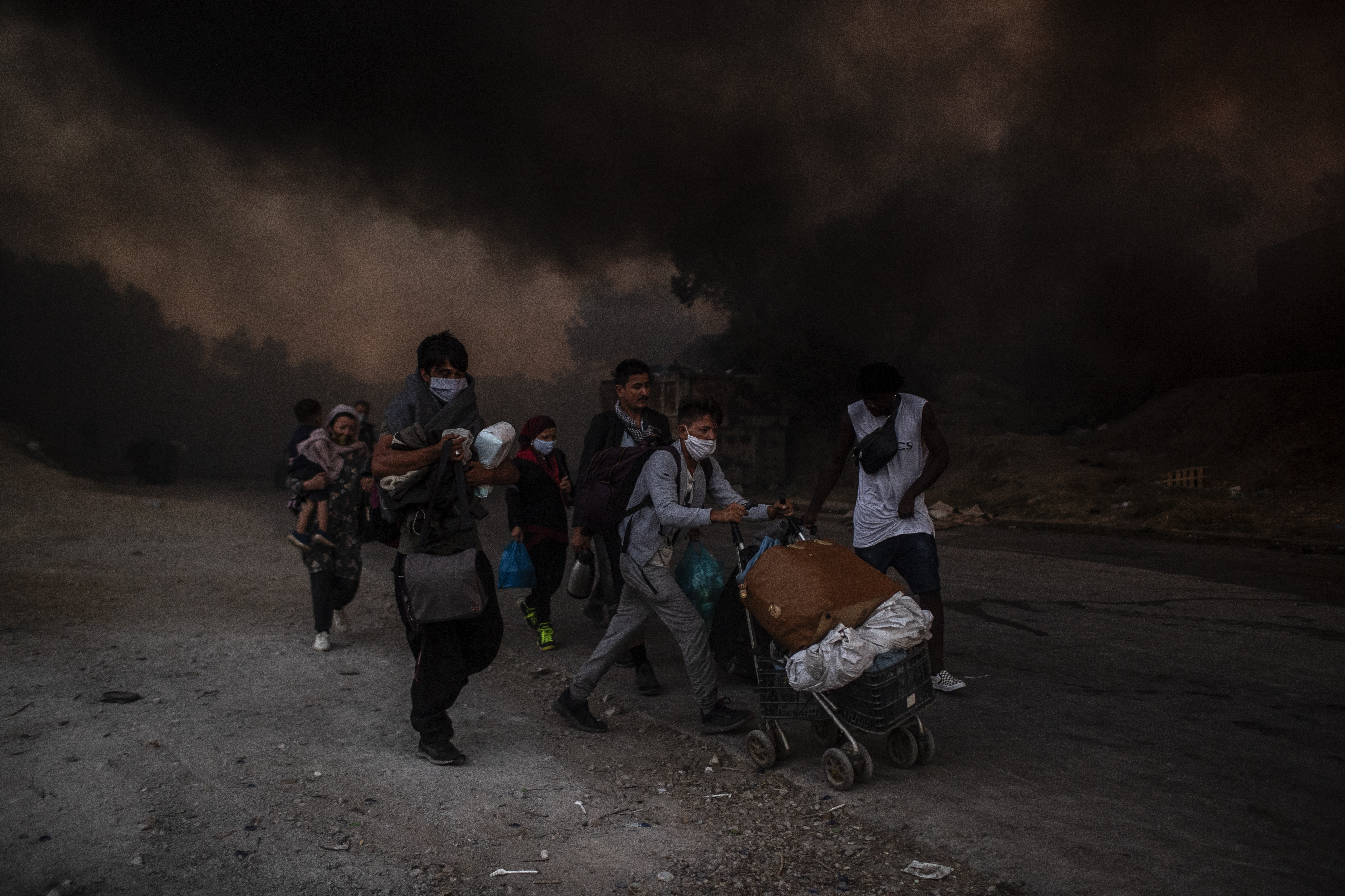 Refugees and migrants carrying their belongings flee a fire burning at the Moria camp on Lesbos island, Greece, Wednesday, Sept. 9, 2020. Moria camp's life ended as it began, in drama: Successive fires that started before dawn on Sept. 9 devastating the site and making 12,000 inhabitants homeless during a COVD-19 lockdown.(AP Photo/Petros Giannakouris)