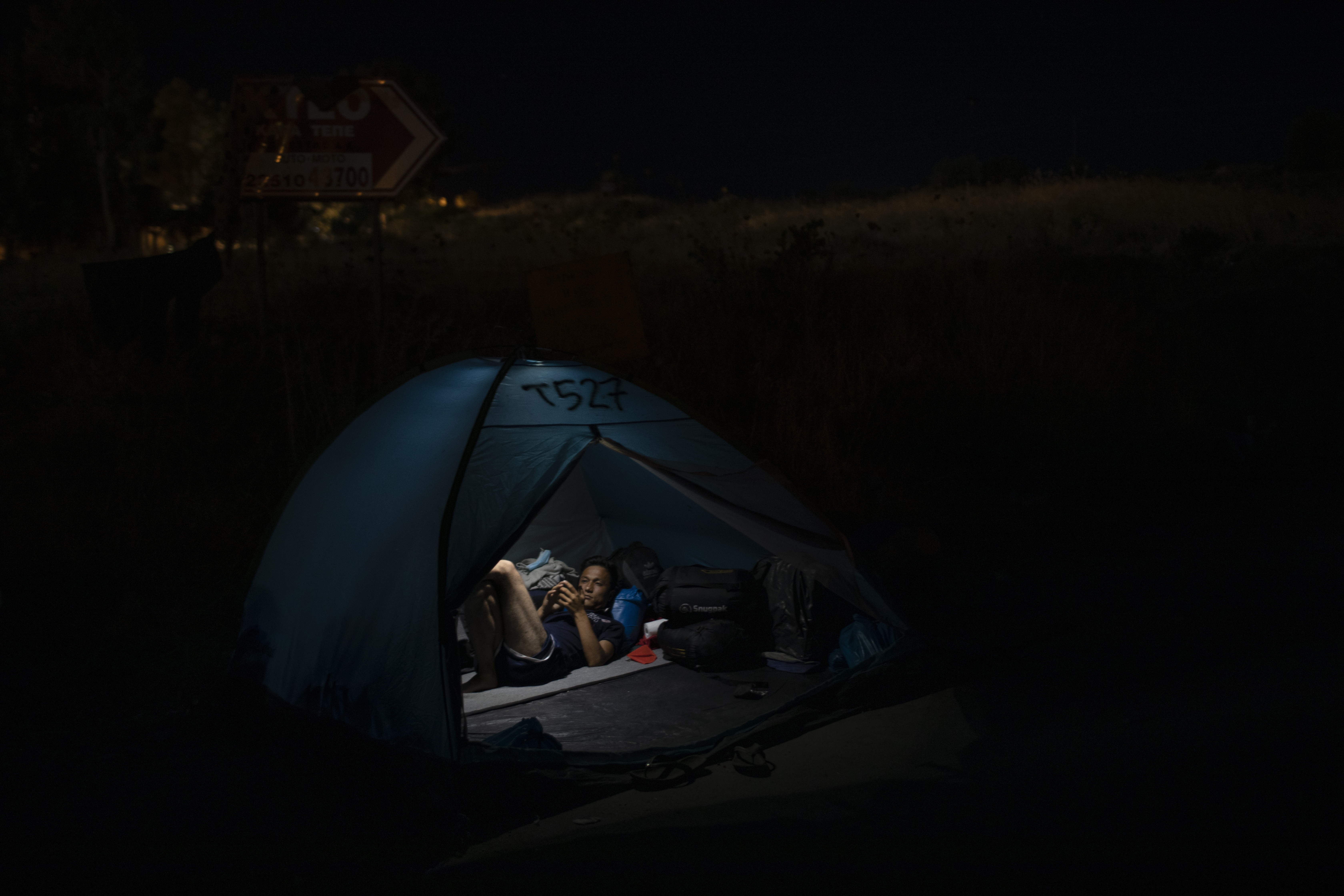 An Afghan man from the destroyed Moria camp , looks at he mobile phone as he rests in a tent, on the road that refugees and migrants are sheltered on, in Lesbos island, Greece, Thursday Sept. 17, 2020. (AP Photo/Petros Giannakouris)