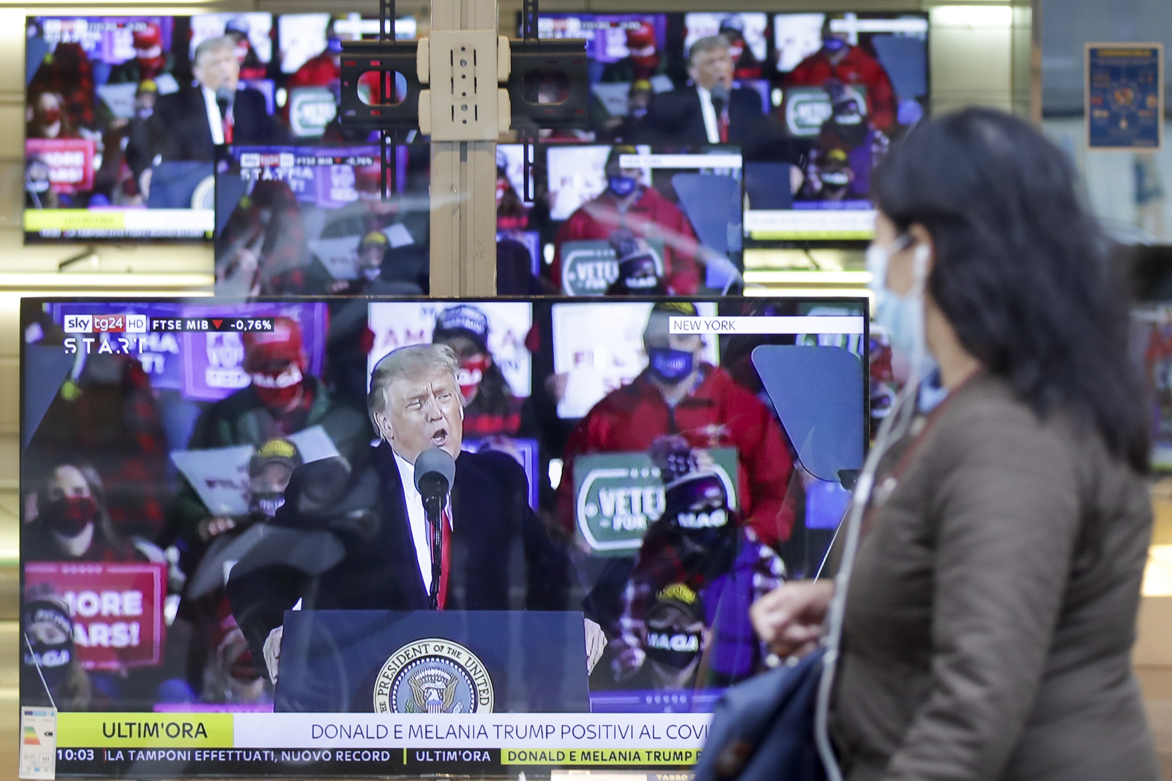 A woman wearing a face mask walks by the window of a shop with TV screens showing an image of U.S. President Donald Trump during a news program, in Milan, Friday, Oct. 2, 2020. Trump said early Friday that he and first lady Melania Trump have tested positive for the coronavirus, a stunning announcement that plunges the country deeper into uncertainty just a month before the presidential election. (AP Photo/Luca Bruno)