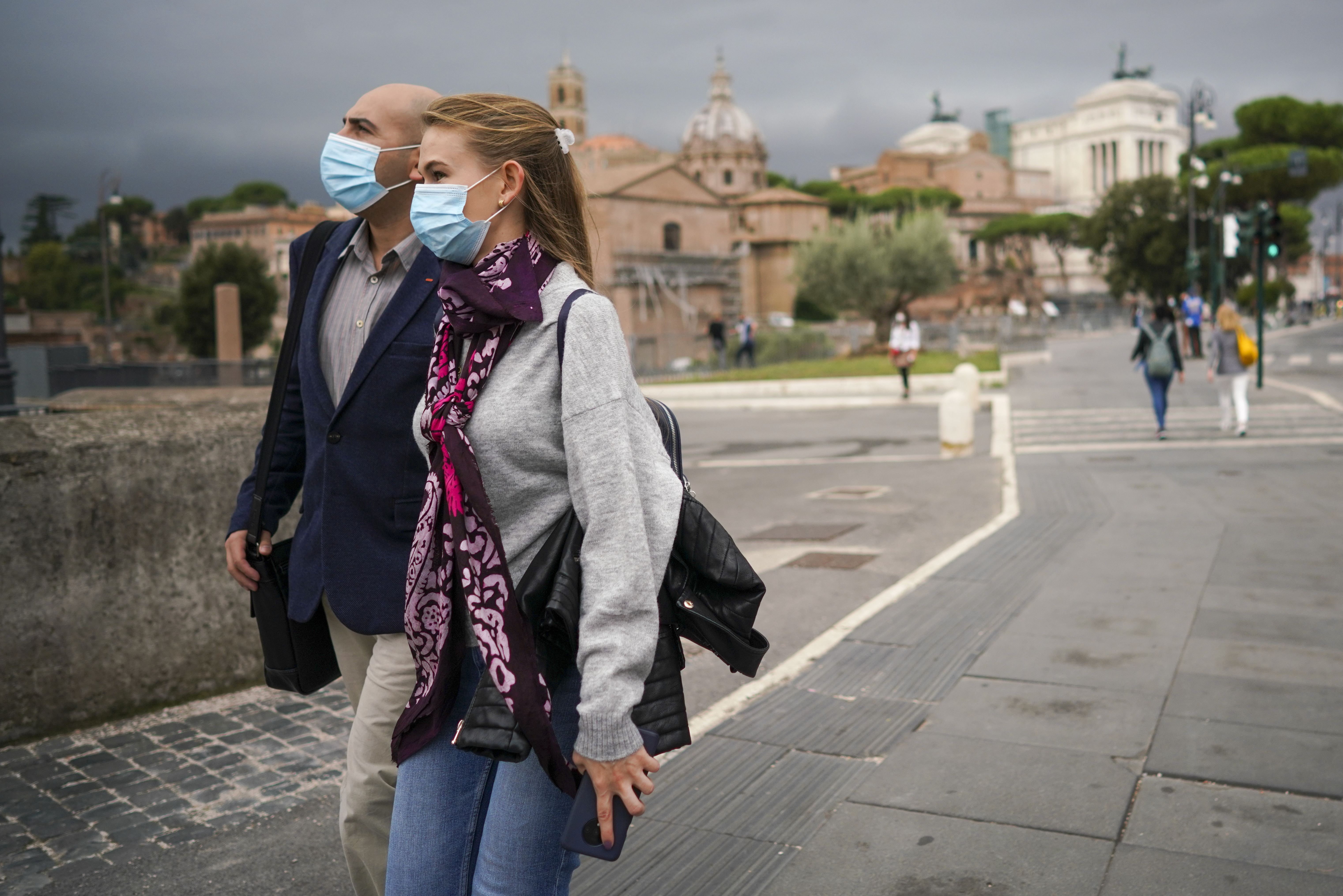 People wear face masks to prevent the spread of COVID-19 as they walk along the Fori Imperiali avenue, in Rome, Saturday, Oct. 3, 2020. As of Saturday it is mandatory to wear masks outdoors in Lazio, the region that includes Rome. (AP Photo/Andrew Medichini)