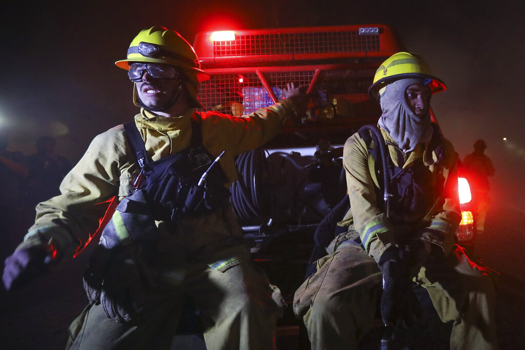 Firefighters sit on a vehicle amid fires in Cordoba, Argentina, late Monday, Oct. 12, 2020. Wildfires have destroyed thousands of hectares in the Argentine province of Cordoba this year, amid a drought and high temperatures. (AP Photo/Nicolas Aguilera)