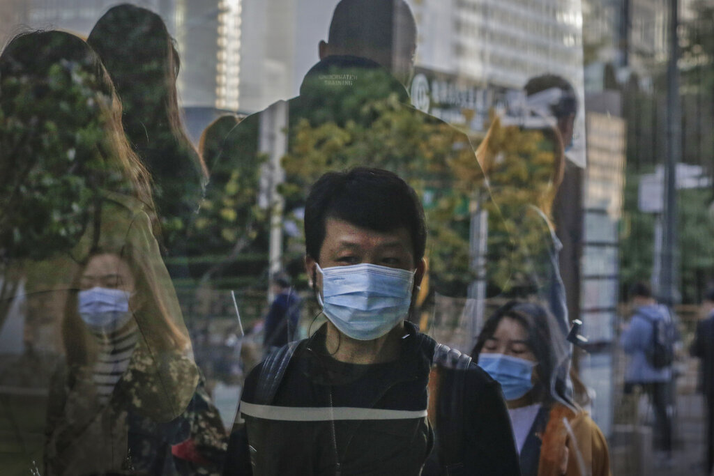 Commuters wearing face masks to help curb the spread of the coronavirus are reflected on a window panel as they walk out from a subway station during the morning rush hour in Beijing, Monday, Oct. 19, 2020. (AP Photo/Andy Wong)