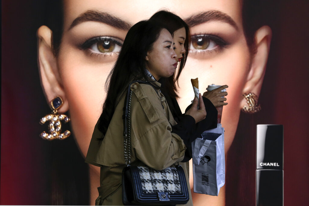 Women eating snack walk by a Chanel cosmetic shop at the capital city's popular shopping mall in Beijing, Monday, Oct. 19, 2020. China’s shaky economic recovery from the coronavirus pandemic is gaining strength as consumers return to shopping malls and auto dealerships while the United States and Europe endure painful contractions.(AP Photo/Andy Wong)