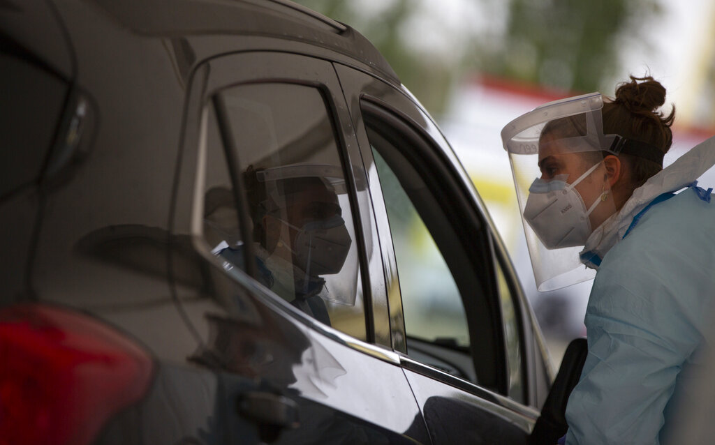 A health care worker speaks with a man in a car as she prepares to administer a nose-swab test at the mobile COVID-19 testing site in Antwerp, Belgium, Tuesday, Oct. 20, 2020. Bars and restaurants across Belgium have been shut down for a month and a night-time curfew entered into force Monday, as health authorities warned of a possible sanitary 