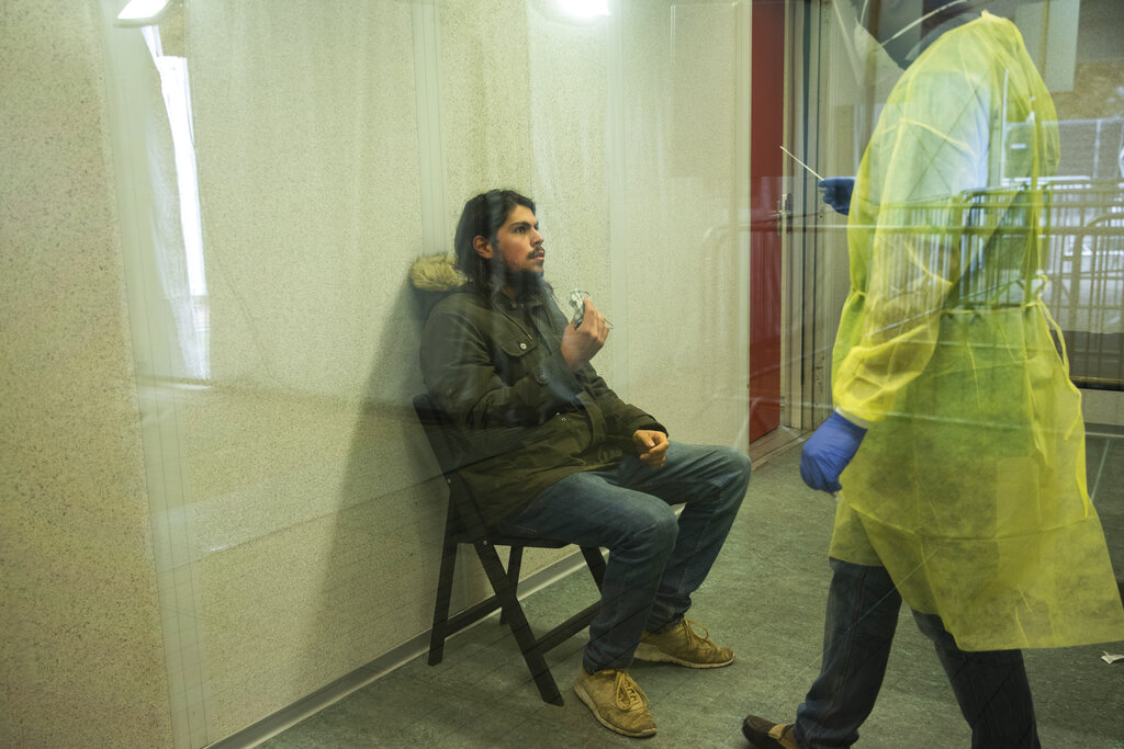 A medical worker, wearing full protective gear, talks to a patient as he takes a nose swab to be tested for COVID-19 in a Red Cross test center in Brussels, Tuesday, Oct. 20, 2020. Bars and restaurants across Belgium shut down for a month and a night-time curfew entered into force Monday in the hard-hit coronavirus country as health authorities warned of a possible sanitary “tsunami.