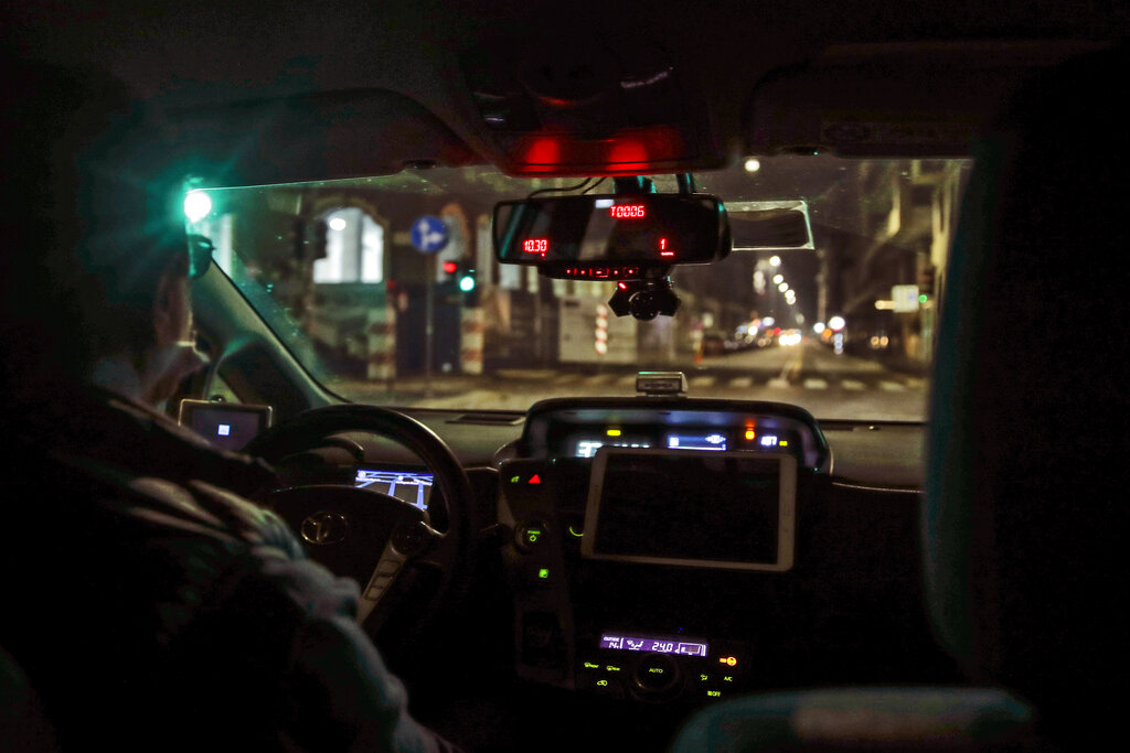 A taxi drives along an empty street in Milan, northern Italy, early Sunday, Oct. 25, 2020. Since the 11 p.m.-5 a.m. curfew took effect last Thursday, people can only move around during those hours for reasons of work, health or necessity.  (AP Photo/Luca Bruno)