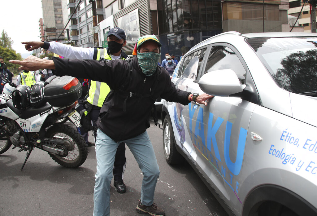 A supporter of Indigenous rights and environmentalist activist Yaku Perez, who is running for president with the Pachakutik political party, and a police officer direct Perez's car away from the Swissotel where international observers from the previous day's presidential elections are staying in Quito, Ecuador, Monday, Feb. 8, 2021. Perez's party gathered here to demand observers be vigilant of the vote count while it is still undecided who will make it to the second-round vote in April, Perez or his rival, a conservative former banker Guillermo Lasso, to run against young leftist Andrés Arauz. (AP Photo/Dolores Ochoa)
