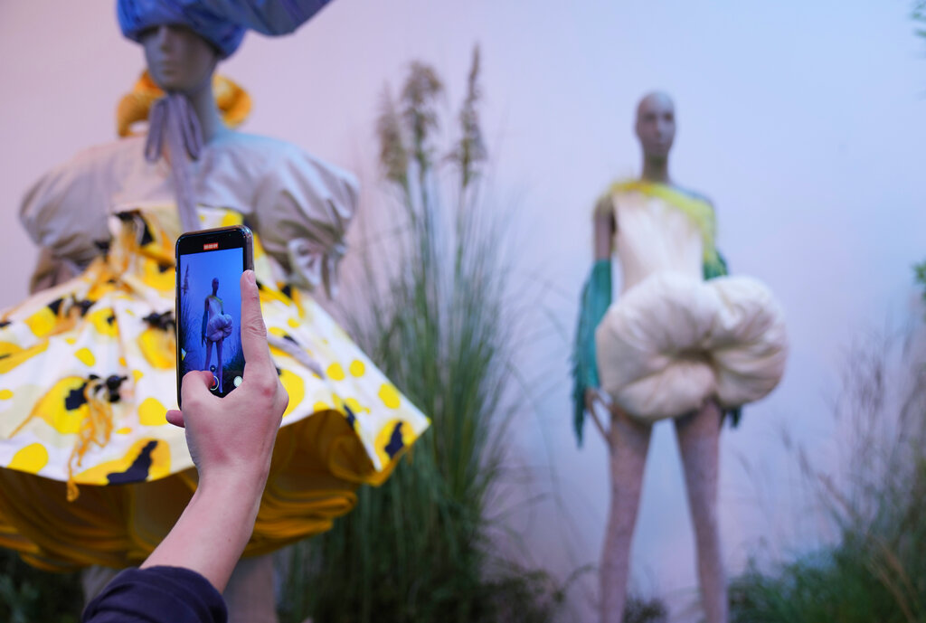 A woman photographs creations by fashion designers Julian Cerro and Jacques Bam, of the Spring Summer 2022 collection, unveiled during the Milan Fashion Week, in Milan, Italy, Tuesday, Sept. 21, 2021. (AP Photo/Antonio Calanni)