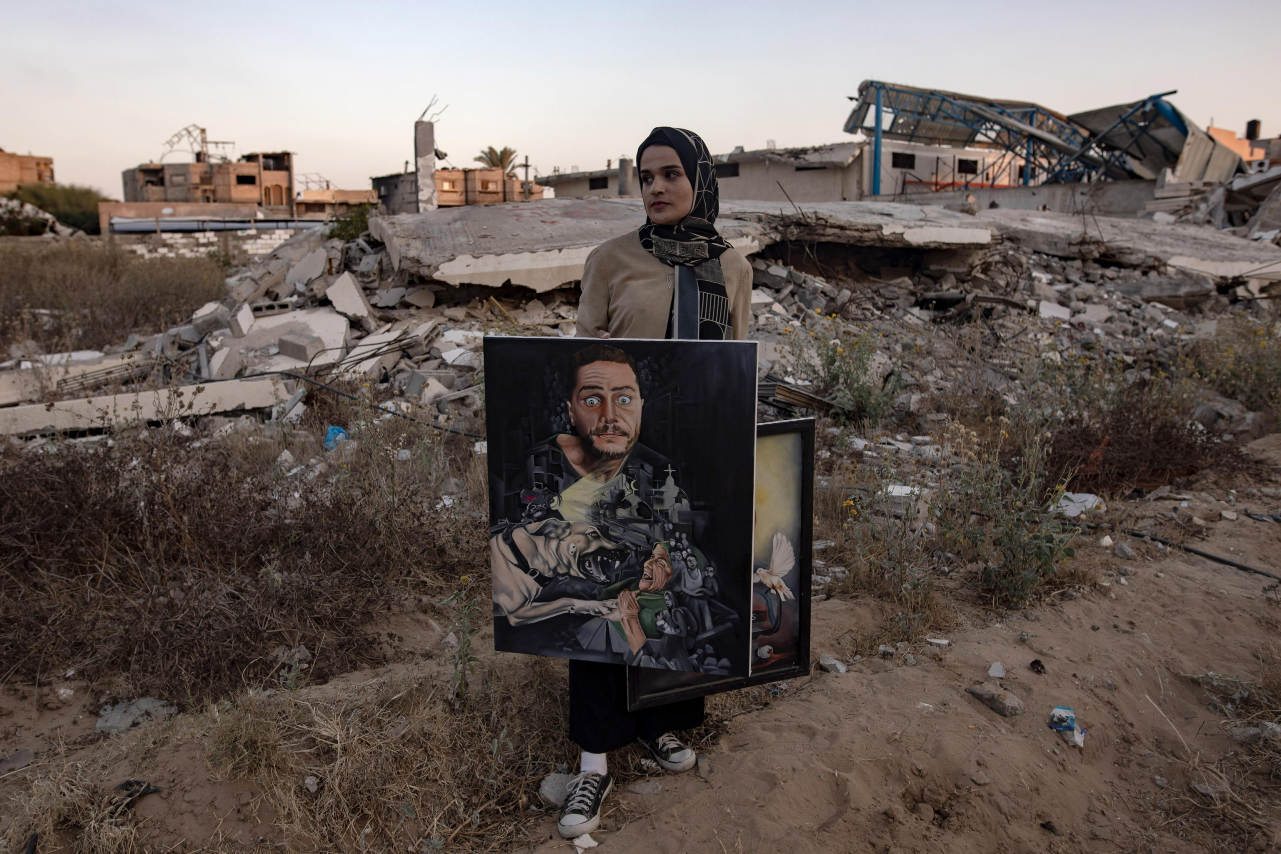 L'artista palestinese Ilham Al-Astal, 28 anni, sfollata dal campo di Al Mawasi, posa con uno dei suoi dipinti vicino alla sua casa distrutta, a Khan Yunis, nel sud della Striscia di Gaza, il 15 luglio 2024. Foto: EPA/HAITHAM IMAD via Ansa