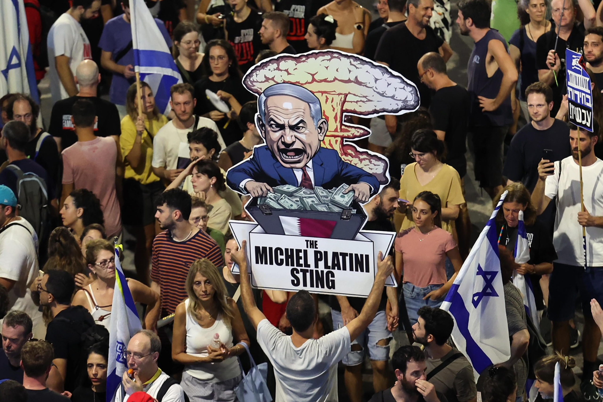 epa11578406 A demonstrator holds up a placard with a caricature of Israeli Prime Minister Benjamin Netanyahu reading 'The Michel Platini Sting' as thousands of demonstrators supporting the families of Israeli hostages held by Hamas in Gaza take part in a protest rally outside the Kyria military headquarters in Tel Aviv, Israel, 01 September 2024. Demonstrators called on Israeli Prime Minister Netanyahu to 'immediately' sign a hostage deal. The Israeli military announced on 01 September that six Israeli hostages - Ori Danino, Alex Lubnov, Hersh Goldberg-Polin, Almog Sarusi, Eden Yerushalmi and Carmel Gat - have been killed by Hamas and were found dead by Israeli forces in an underground tunnel in the Gaza Strip. According to the Israeli Defence Forces (IDF), 101 Israeli hostages remain in captivity in the Palestinian enclave. Israeli trade unionist chairman of Histadrut, Arnon Bar-David, called for a general strike starting 02 September following the news of the death of the six abductees. Rallies in Israel have been critical of the Israeli government's handling of the crisis, demanding the immediate release of all hostages.  EPA/ABIR SULTAN