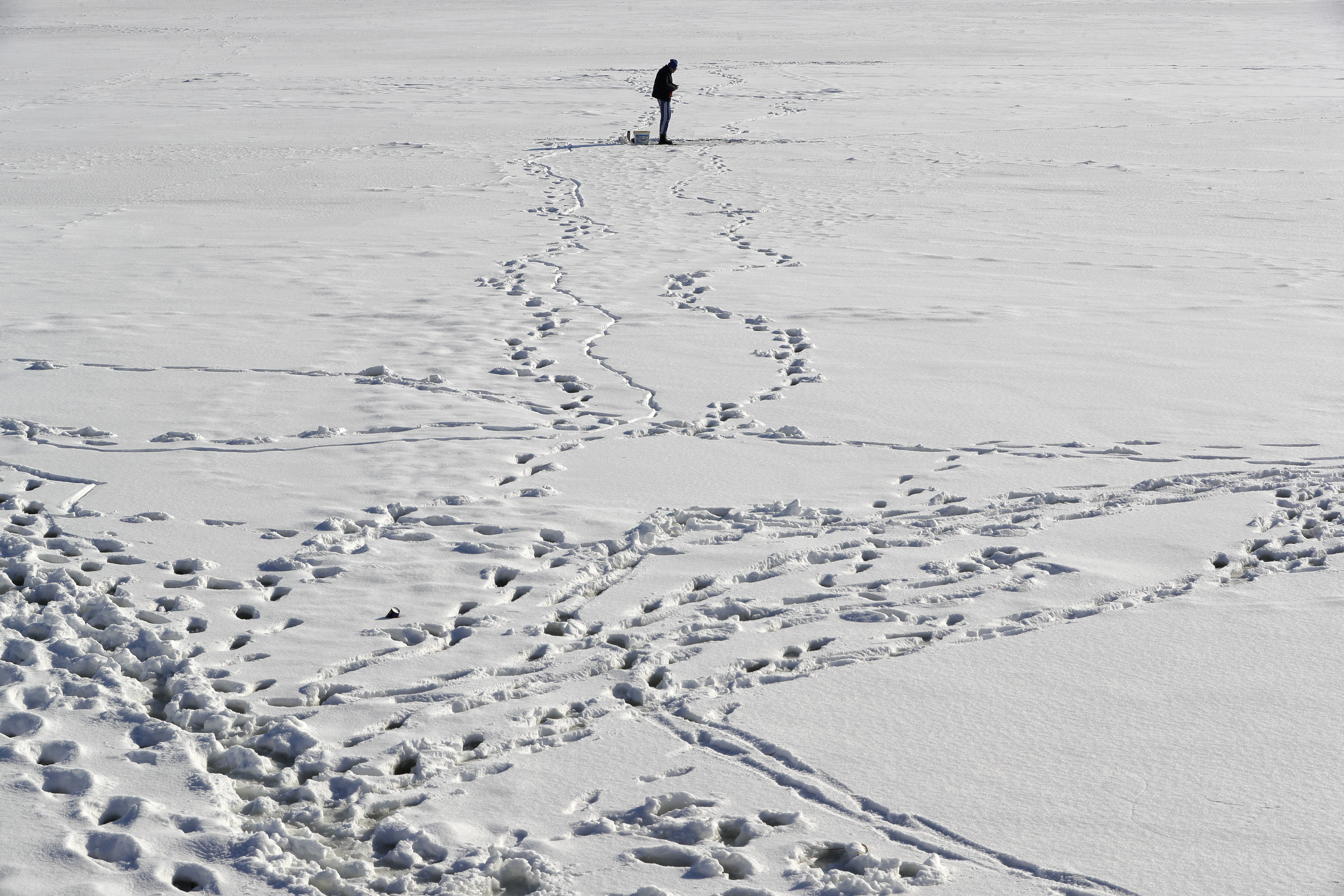 A man fishes on a frozen lake on the outskirts of Bucharest, Romania, Friday, Jan. 13, 2017. The Romanian capital experienced milder weather after a week of blizzards and extreme cold that caused a major disruption of the road and railway transport.(AP Photo/Vadim Ghirda)