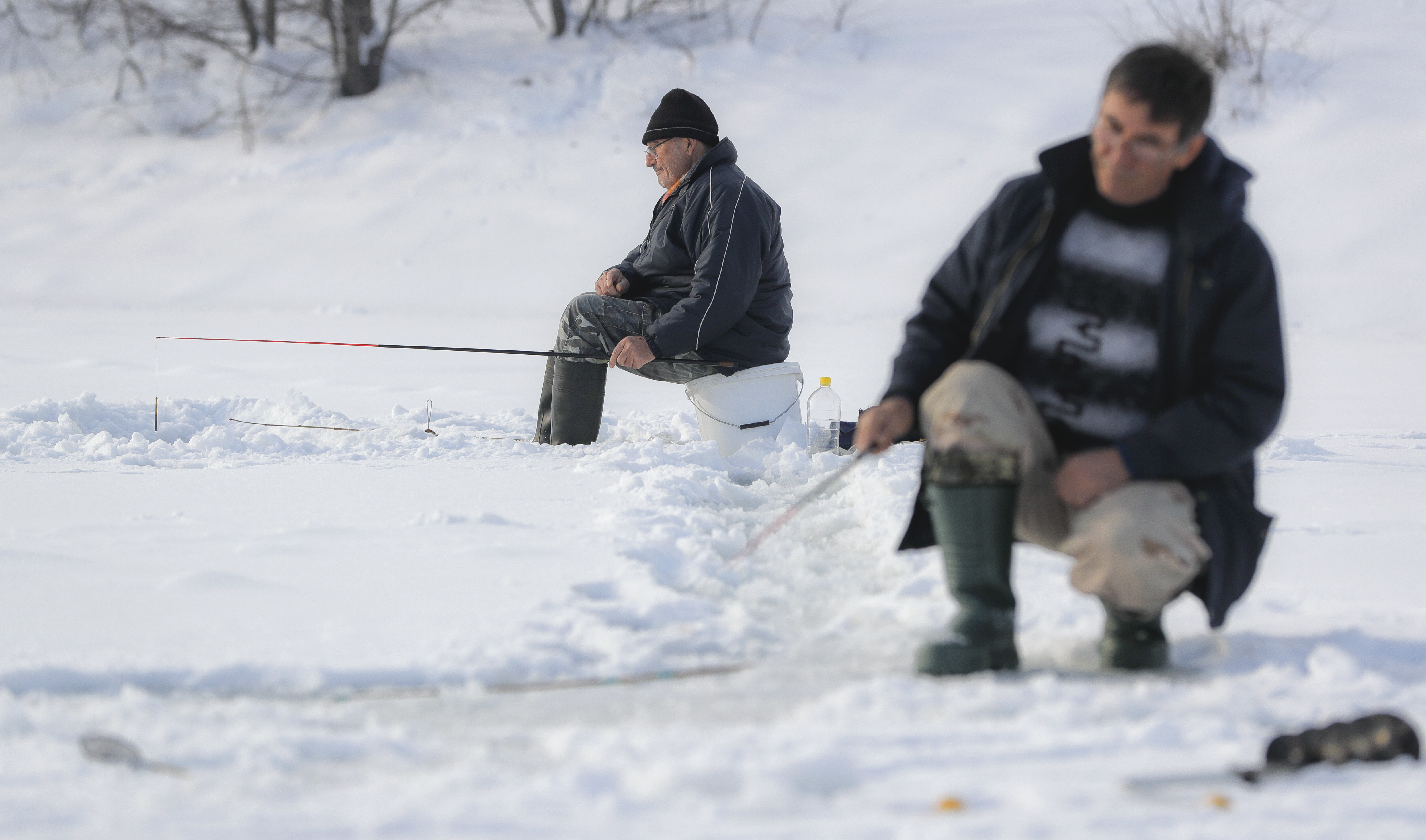 People fish on a frozen lake on the outskirts of Bucharest, Romania, Friday, Jan. 13, 2017. The Romanian capital experienced milder weather after a week of blizzards and extreme cold that caused a major disruption of the road and railway transport. (AP Photo/Vadim Ghirda)