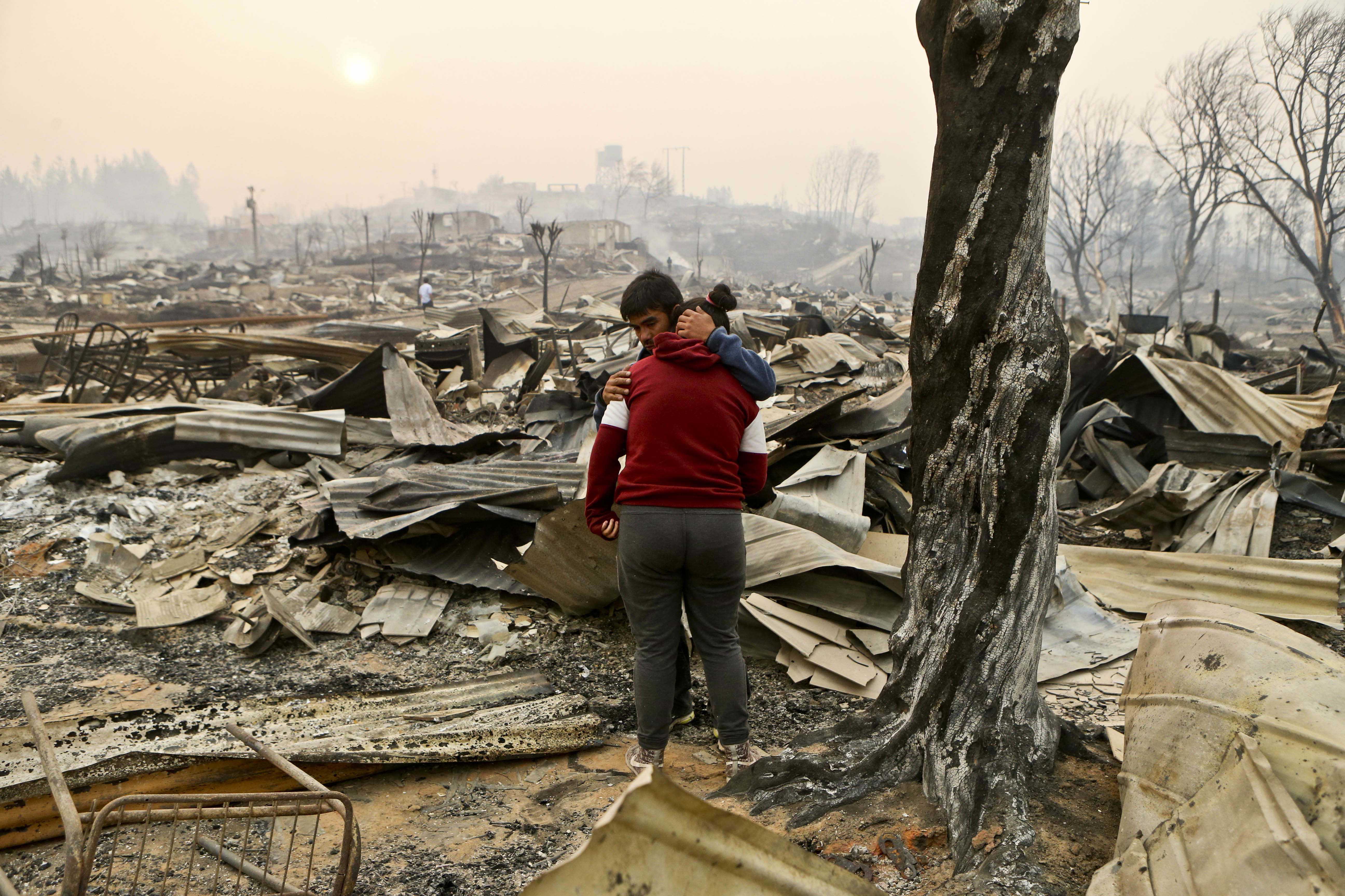Juan Vega embraces his daughter where their home once stood after a wildfire in Santa Olga, Chile, Thursday, Jan. 26, 2017. Officials say the town was consumed by the country's worst wildfires, engulfing the post office, a kindergarten and hundreds of homes. (AP Photo/Esteban Felix)