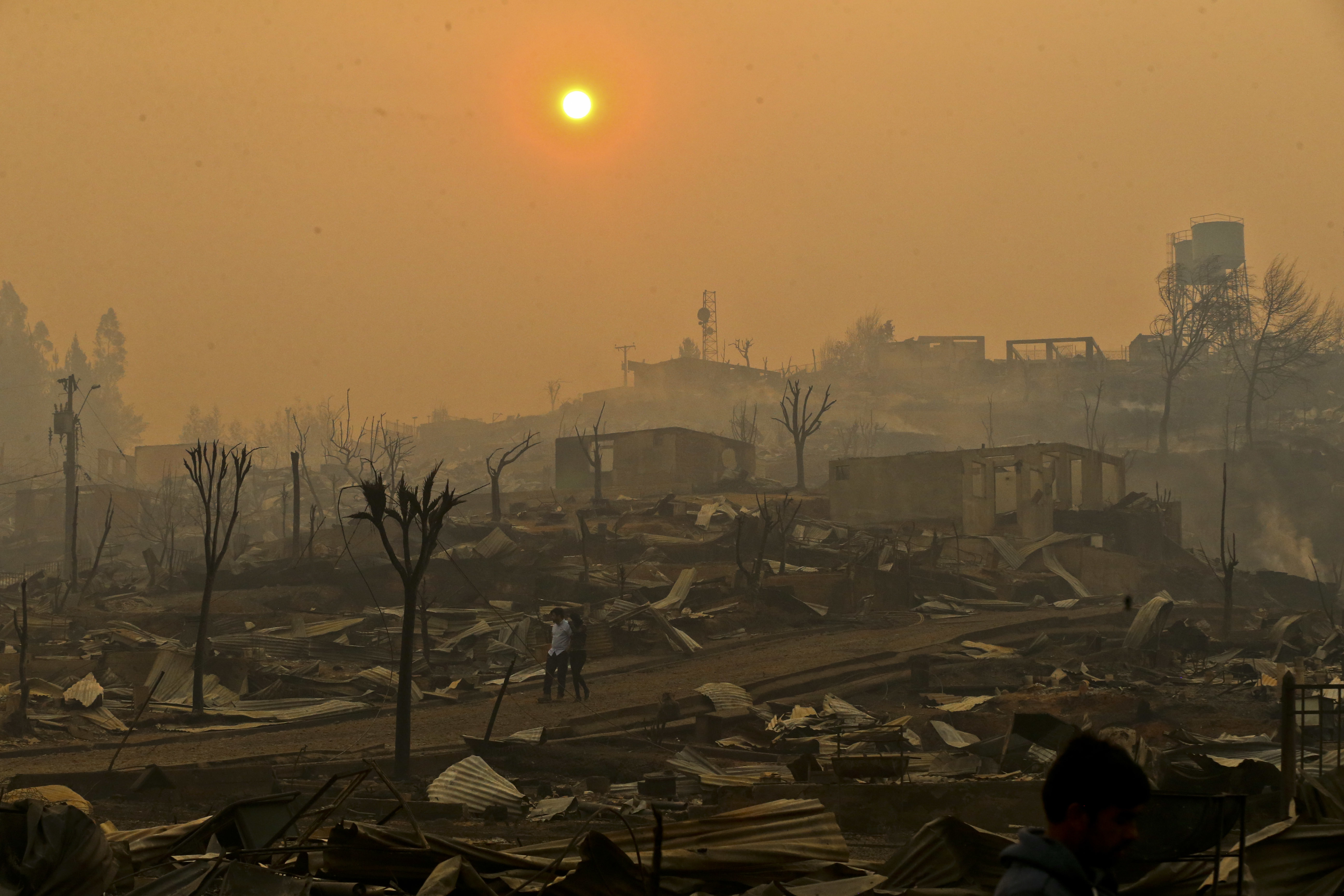 A couple walks through a neighborhood destroyed by fire in Santa Olga, Chile, Thursday, Jan. 26, 2017. Officials say the town was consumed by the country's worst wildfires, engulfing the post office, a kindergarten and hundreds of homes. (AP Photo/Esteban Felix)