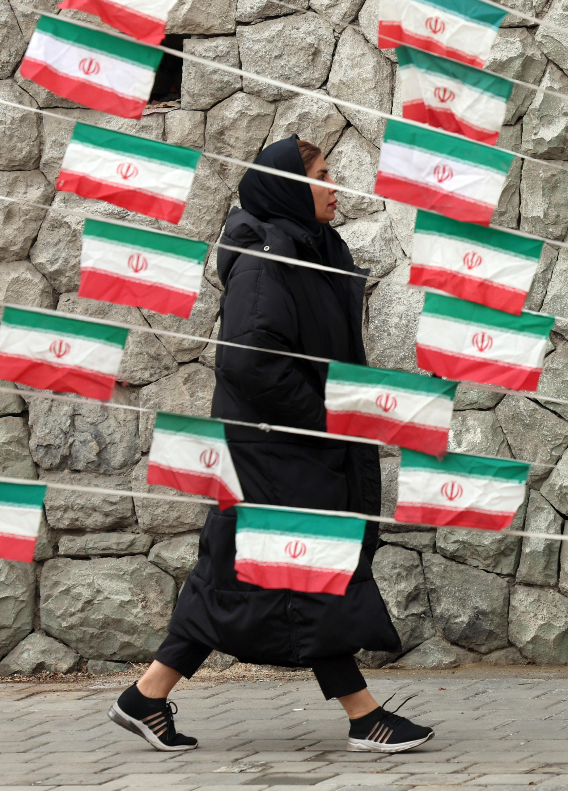 epa11865378 An Iranian woman walks past Iran's national flags as the country marks the 46th anniversary of Khomeini's return from his Paris exile, in Tehran, Iran, 31 January 2025. Iran will celebrate its 45th revolution anniversary on 10 February 2025.  EPA/ABEDIN TAHERKENAREH