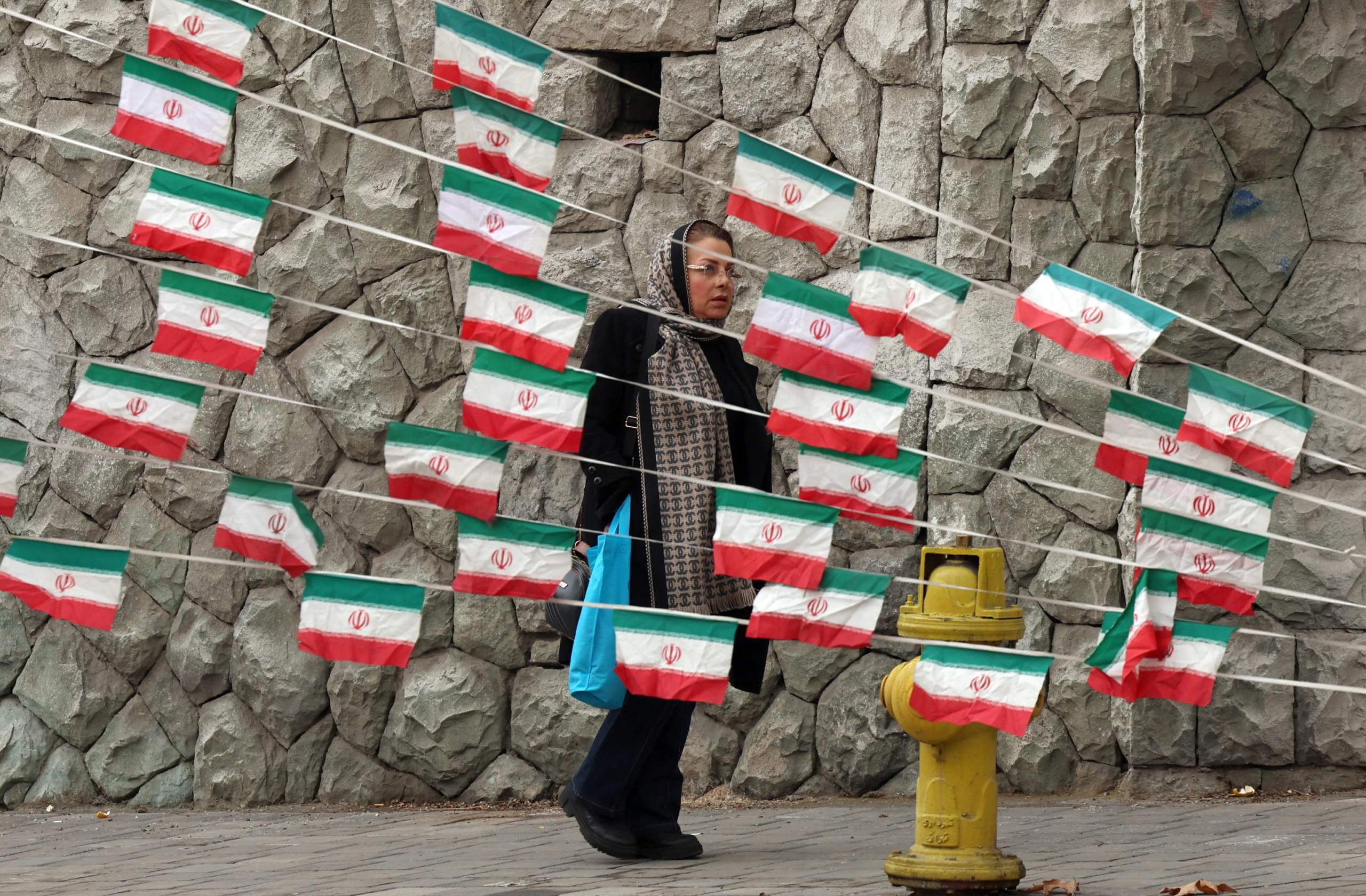 epa11865377 An Iranian woman walks past Iran's national flags as the country marks the 46th anniversary of Khomeini's return from his Paris exile, in Tehran, Iran, 31 January 2025. Iran will celebrate its 45th revolution anniversary on 10 February 2025.  EPA/ABEDIN TAHERKENAREH