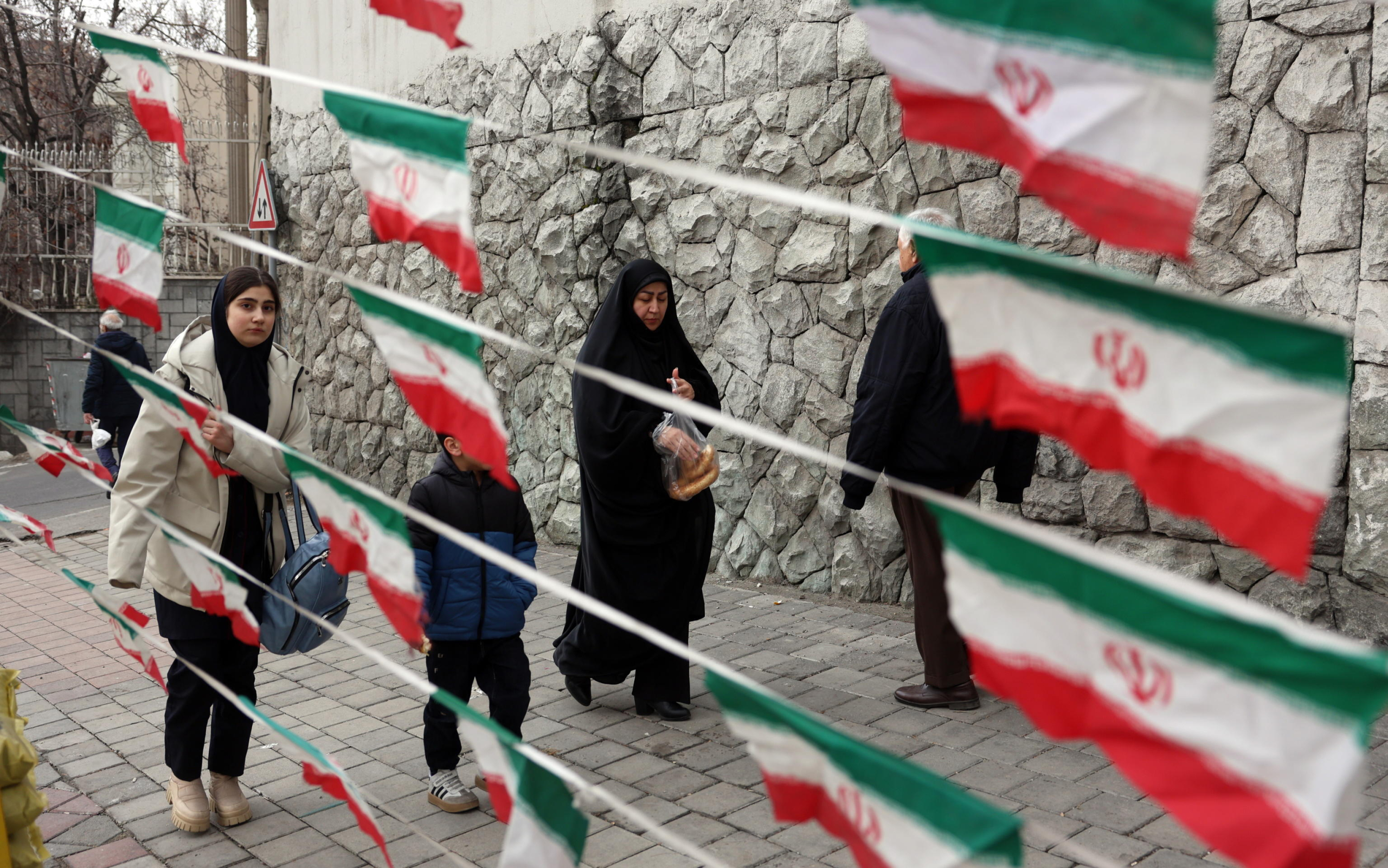 epa11865384 Iranian women walk past Iran's national flags as the country marks the 46th anniversary of Khomeini's return from his Paris exile, in Tehran, Iran, 31 January 2025. Iran will celebrate its 45th revolution anniversary on 10 February 2025.  EPA/ABEDIN TAHERKENAREH