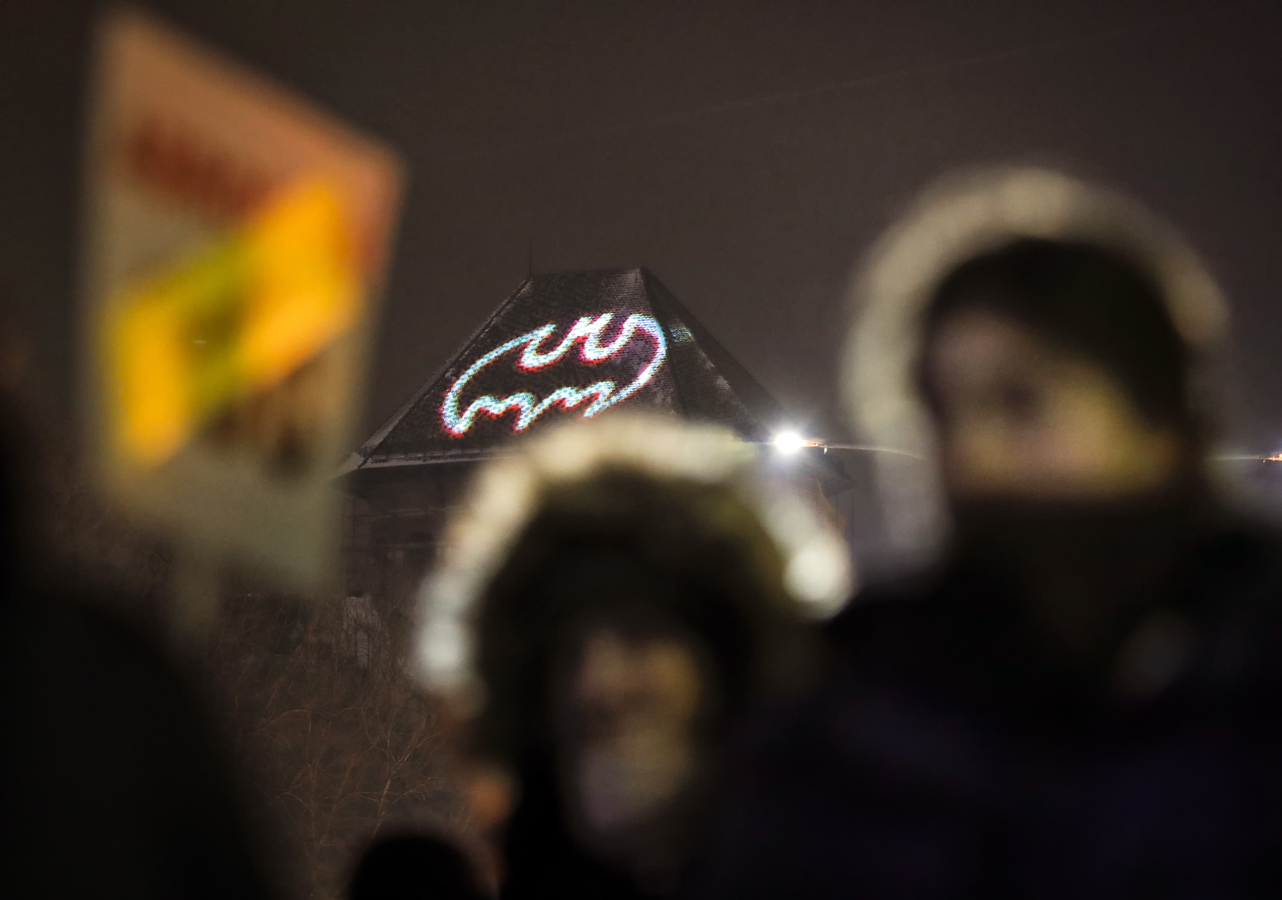 Anti-government protesters hold banners backdropped by a Batman sign projected on a building overlooking the Victory Square outside the government headquarters in Bucharest, Romania, Thursday, Feb. 9, 2017. Romania's justice minister resigned Thursday following mass protests over a law that eases criminal penalties for government officials engaged in corruption.(AP Photo/Vadim Ghirda)